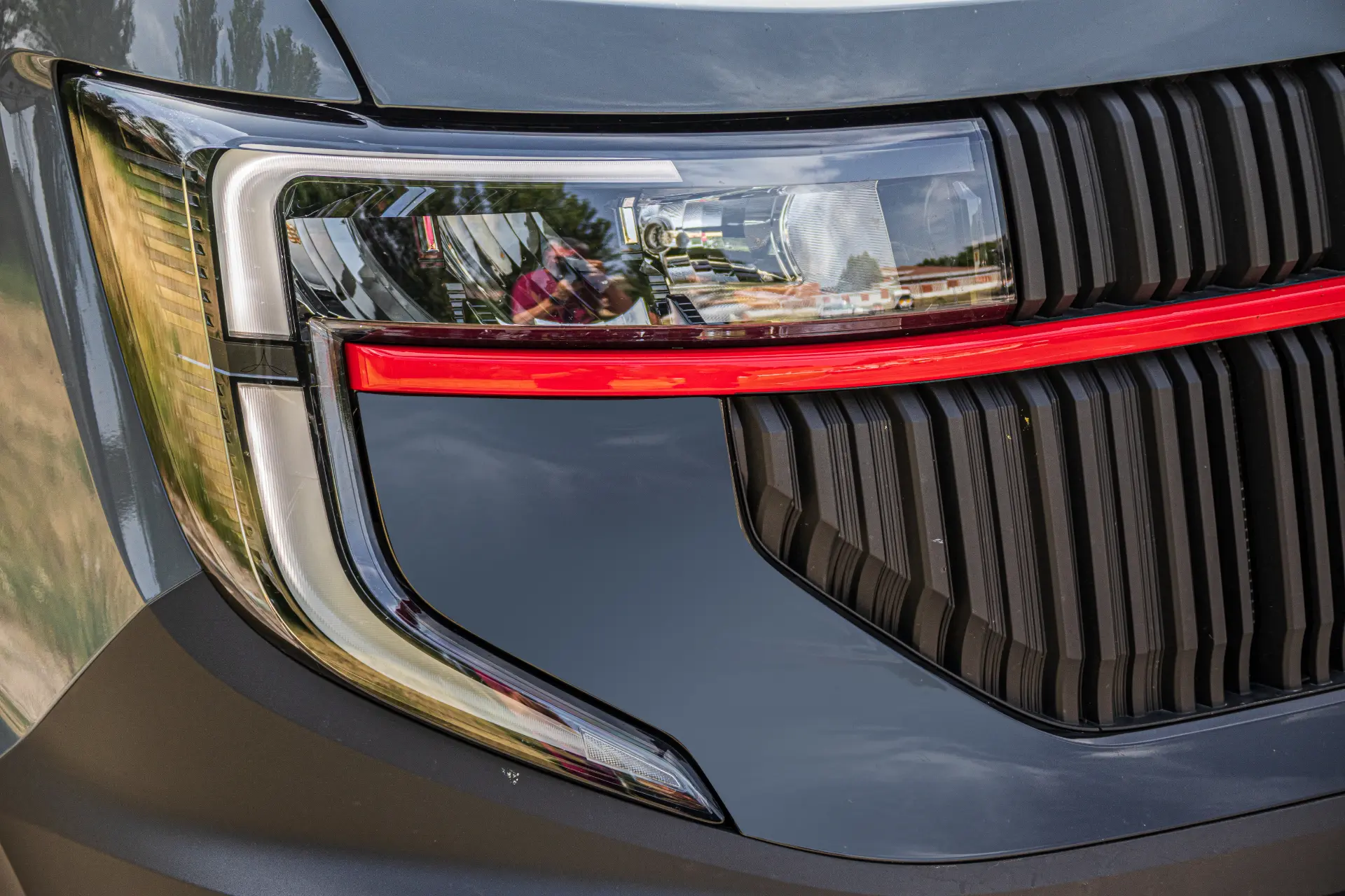 Primer plano del moderno faro de un furgón Renault Master con una franja roja de acento y detalles negros en la parrilla, que ponen de relieve el innovador diseño de las furgonetas eléctricas actuales.