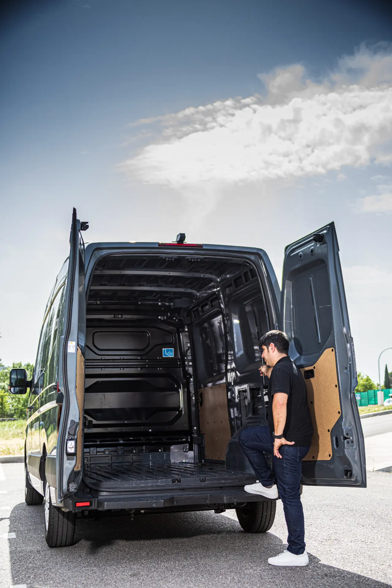 Un hombre permanece junto a las puertas traseras abiertas de una furgoneta Renault Trucks Master E-Tech L3H2 negra vacía, bajo un cielo parcialmente nublado, quizás preparándose para una prueba.