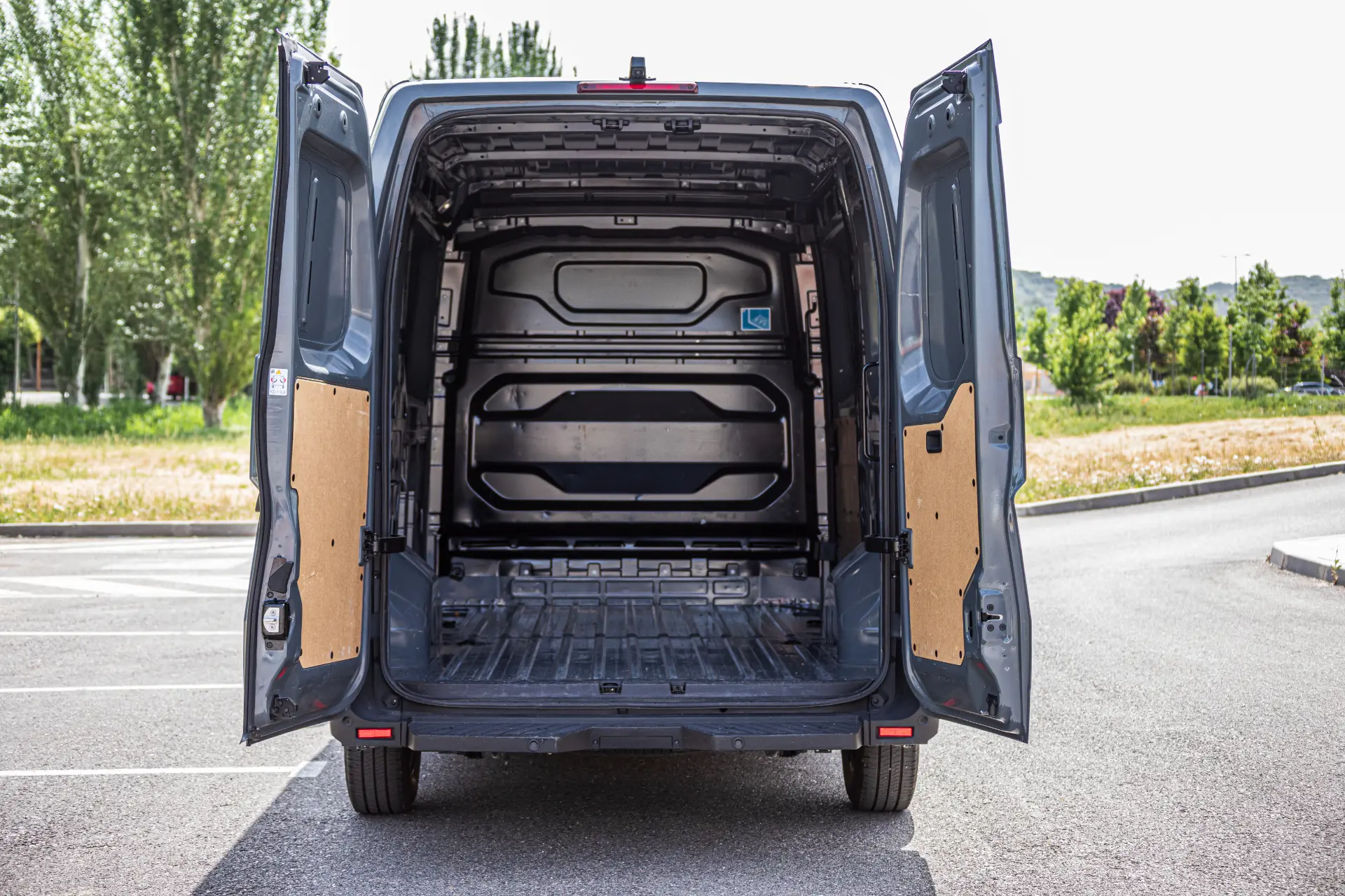 Compartimento de carga vacío de un Renault Trucks Master E-Tech L3H2 gris con las dos puertas traseras abiertas, aparcado en un aparcamiento exterior para pruebas.