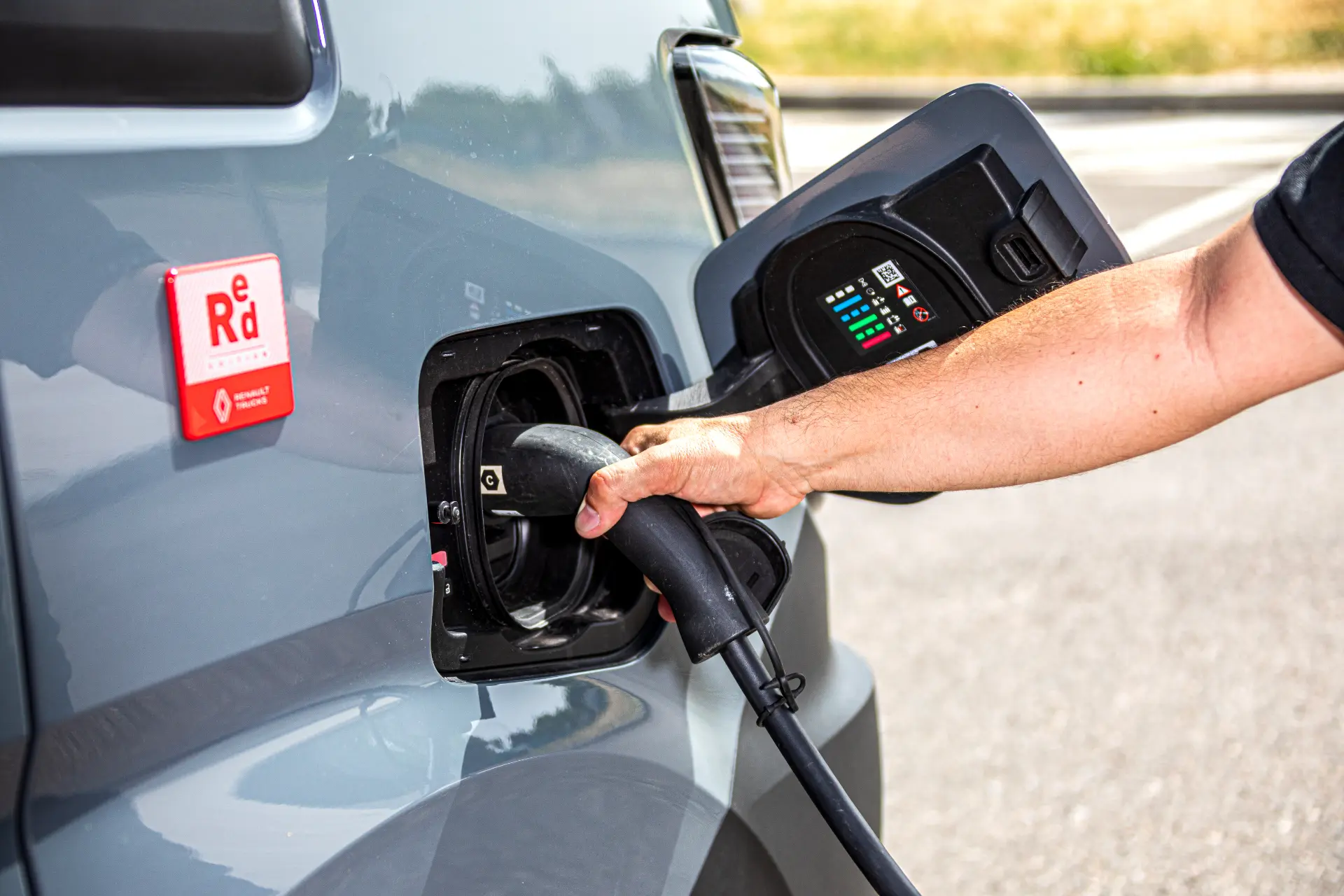 Una persona enchufa un cable de carga a un vehículo eléctrico Renault Trucks Master E-Tech L3H2 en una estación de carga durante una prueba.