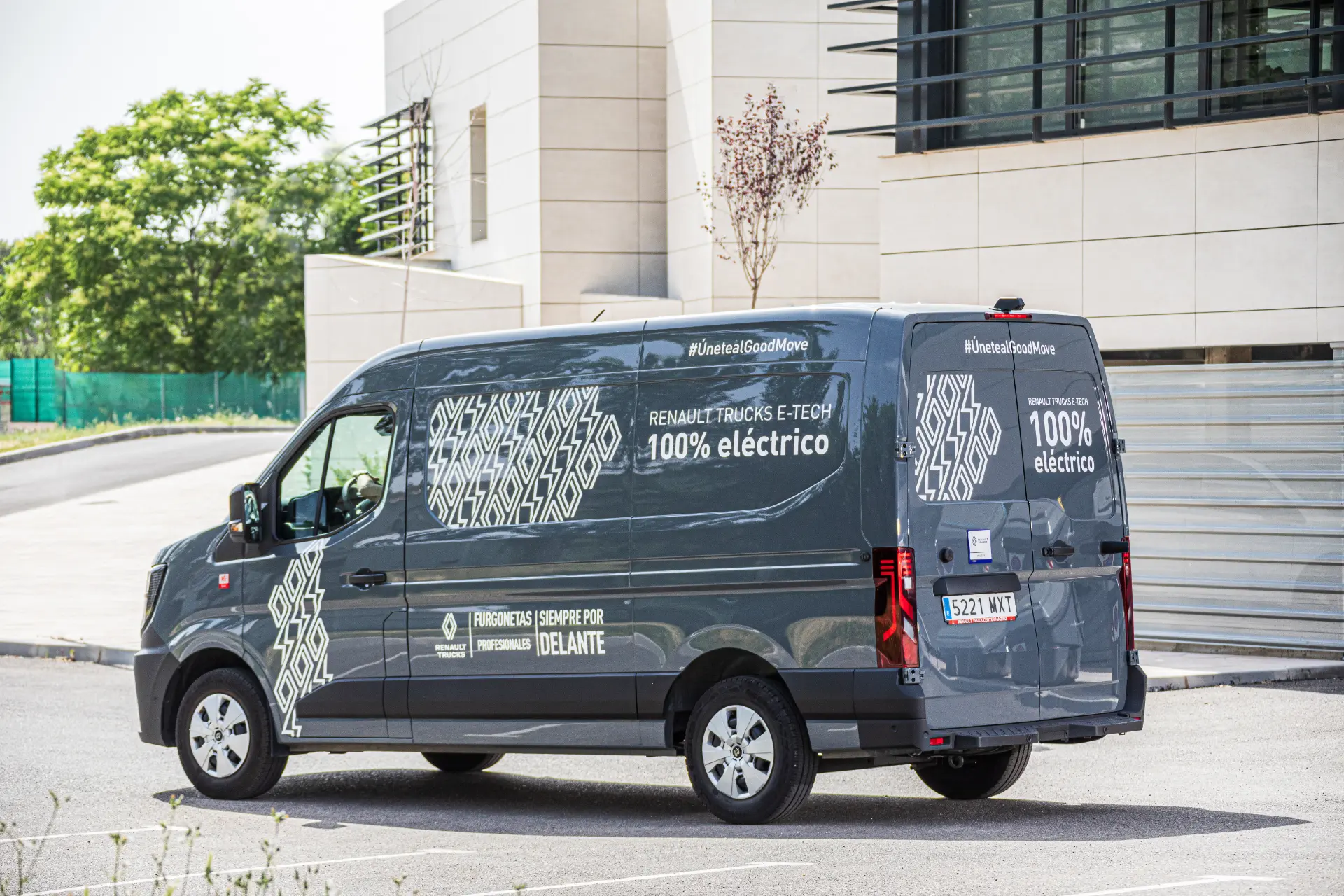 Una furgoneta de reparto eléctrica Renault Trucks Master E-Tech L3H2 gris está aparcada frente a un moderno edificio en un día soleado, lista para su próxima prueba.