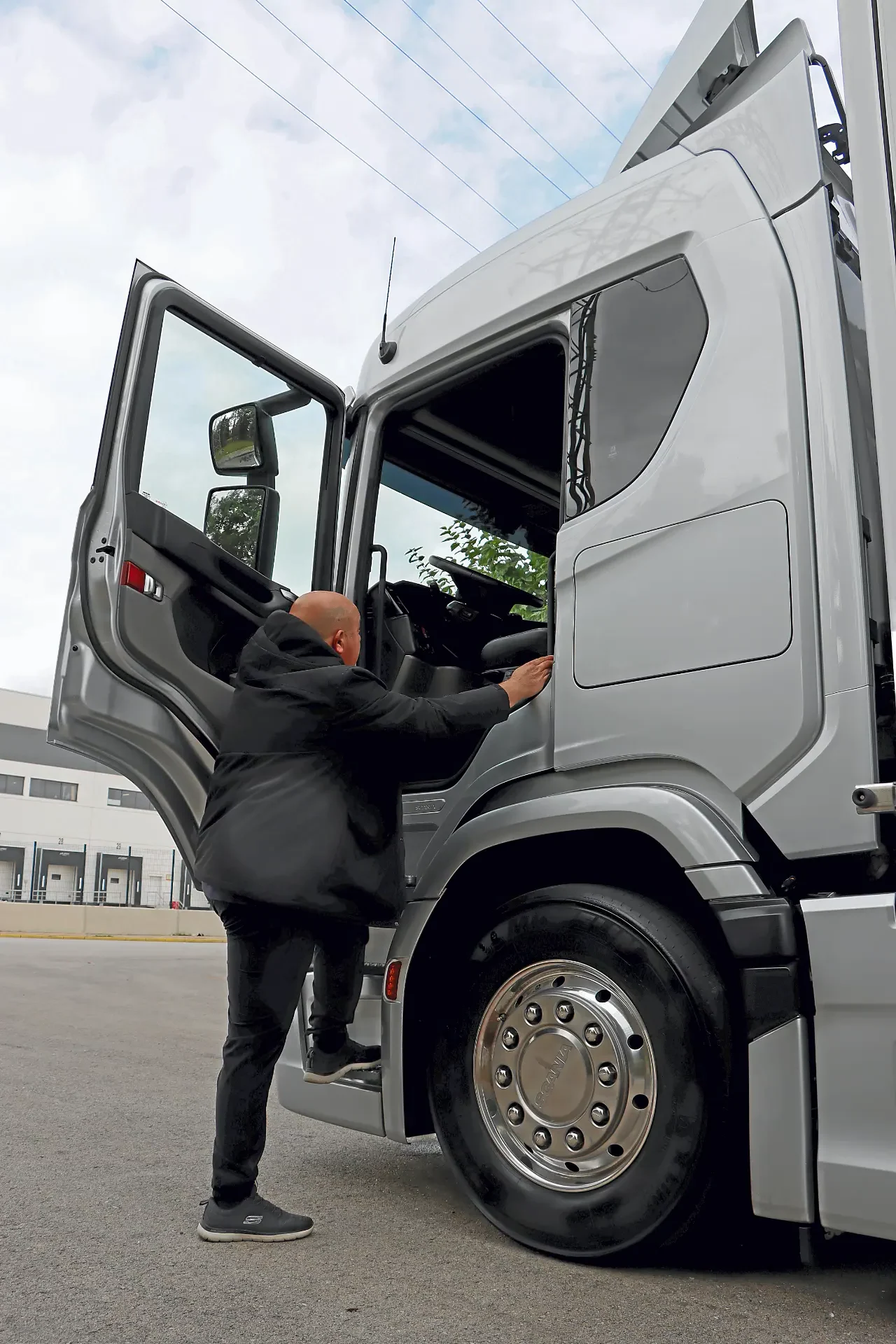 Una persona con traje sube a la cabina de un gran semirremolque plateado aparcado fuera, preparándose para una prueba Scania para evaluar el consumo camiones Scania en condiciones reales.