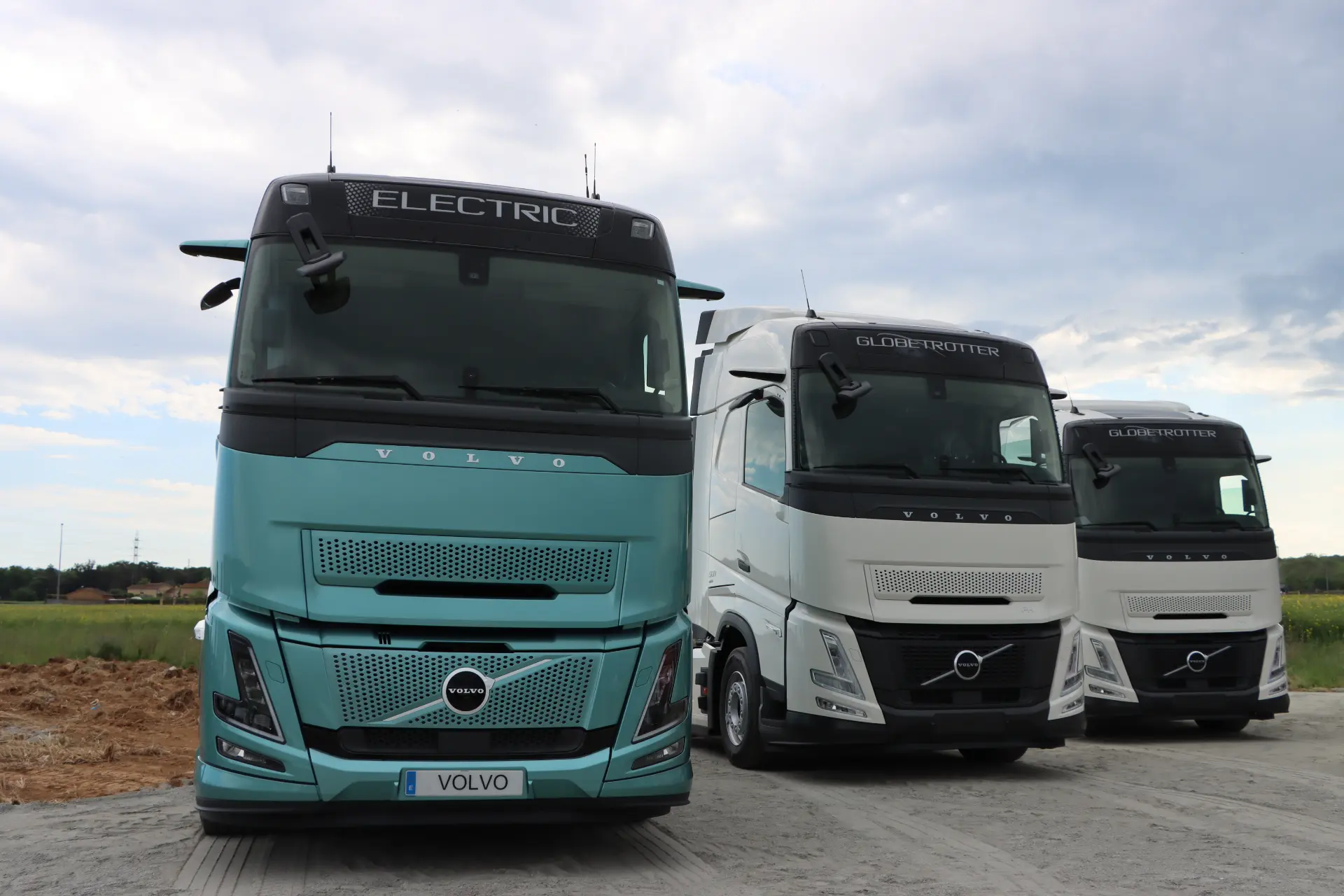 Tres Volvo Trucks, entre ellos uno con la etiqueta "Eléctrico", están aparcados al aire libre sobre una superficie de hormigón en el Truck Center de Girona.