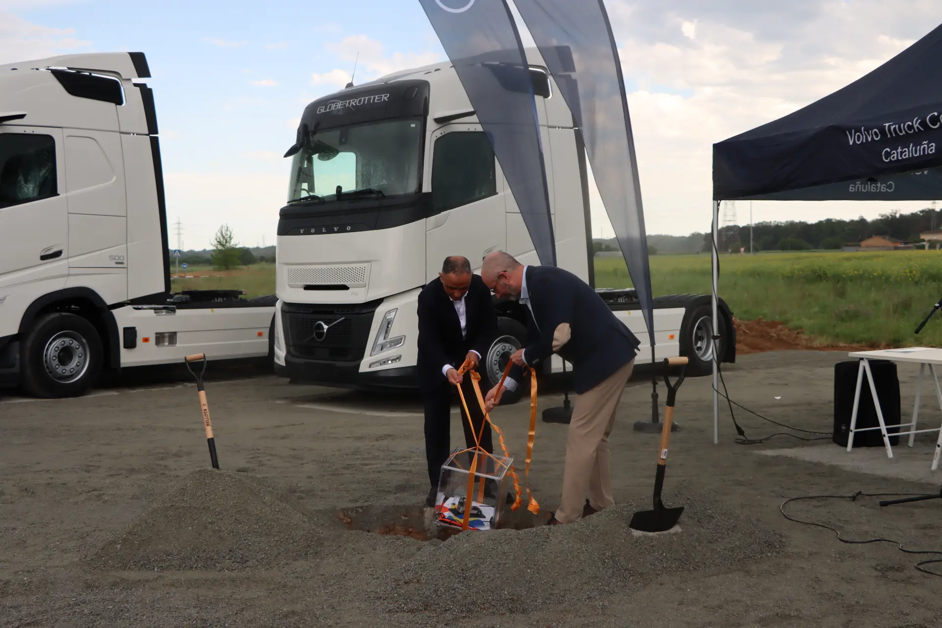 Dos hombres trajeados rompen el suelo con palas delante de Volvo Trucks en un acto al aire libre en Bescanó, marcando el inicio de la construcción del nuevo Truck Center Girona.