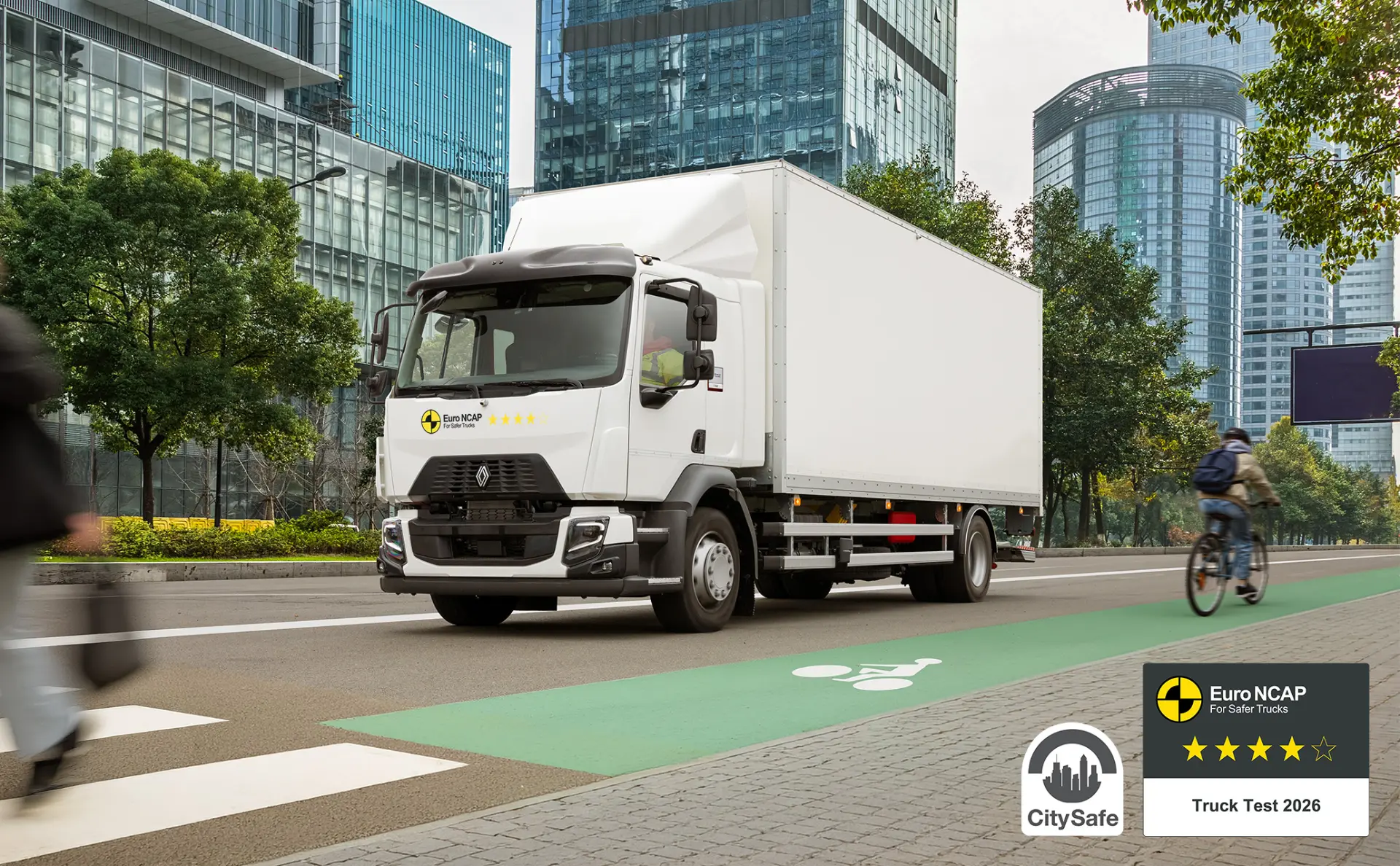 Un camión Renault Trucks D de caja blanca circula por una calle de la ciudad con los distintivos de seguridad CitySafe y Euro NCAP en la esquina.