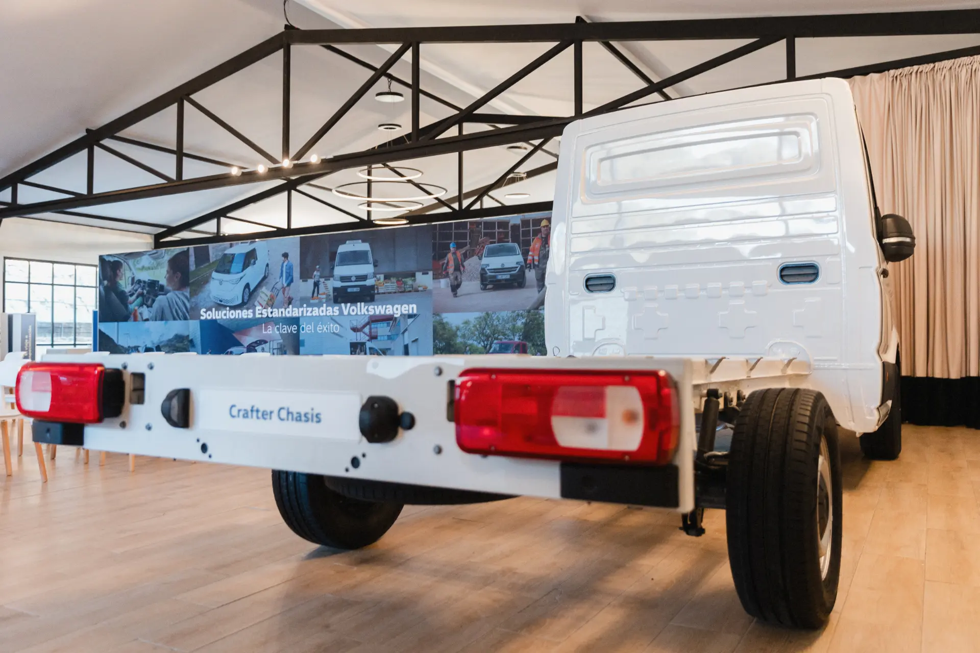 Un vehículo Volkswagen Crafter Chasis blanco expuesto en el interior con una pancarta promocional al fondo, que incorpora el sistema Borrador automático para mejorar la eficiencia.