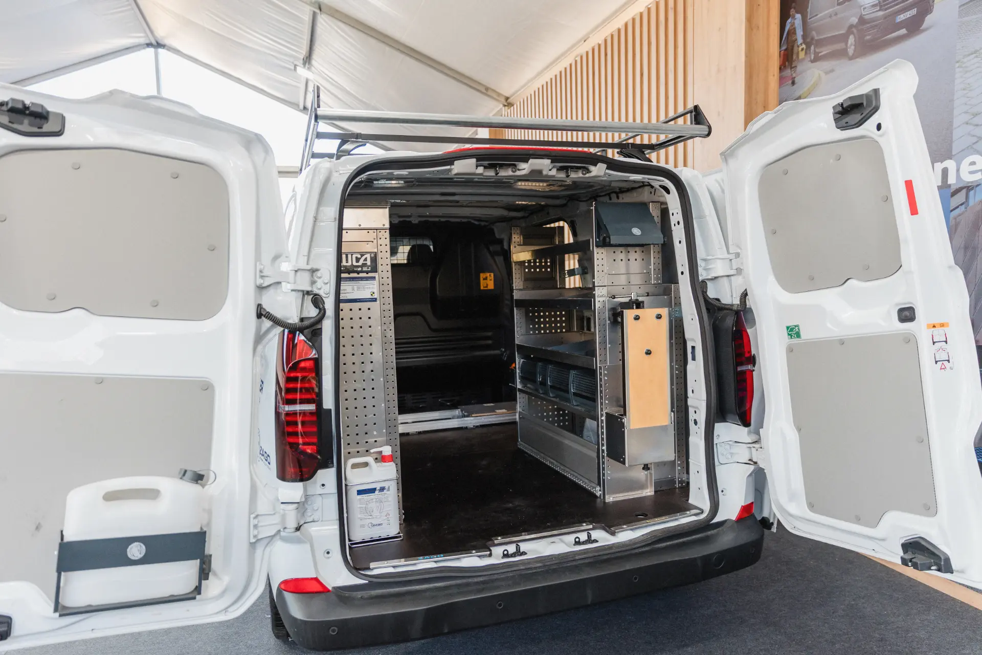 Furgoneta de carga blanca con las puertas traseras abiertas que dejan ver estanterías organizadas, compartimentos de almacenamiento y un borrador automático colocado ordenadamente entre los suministros.