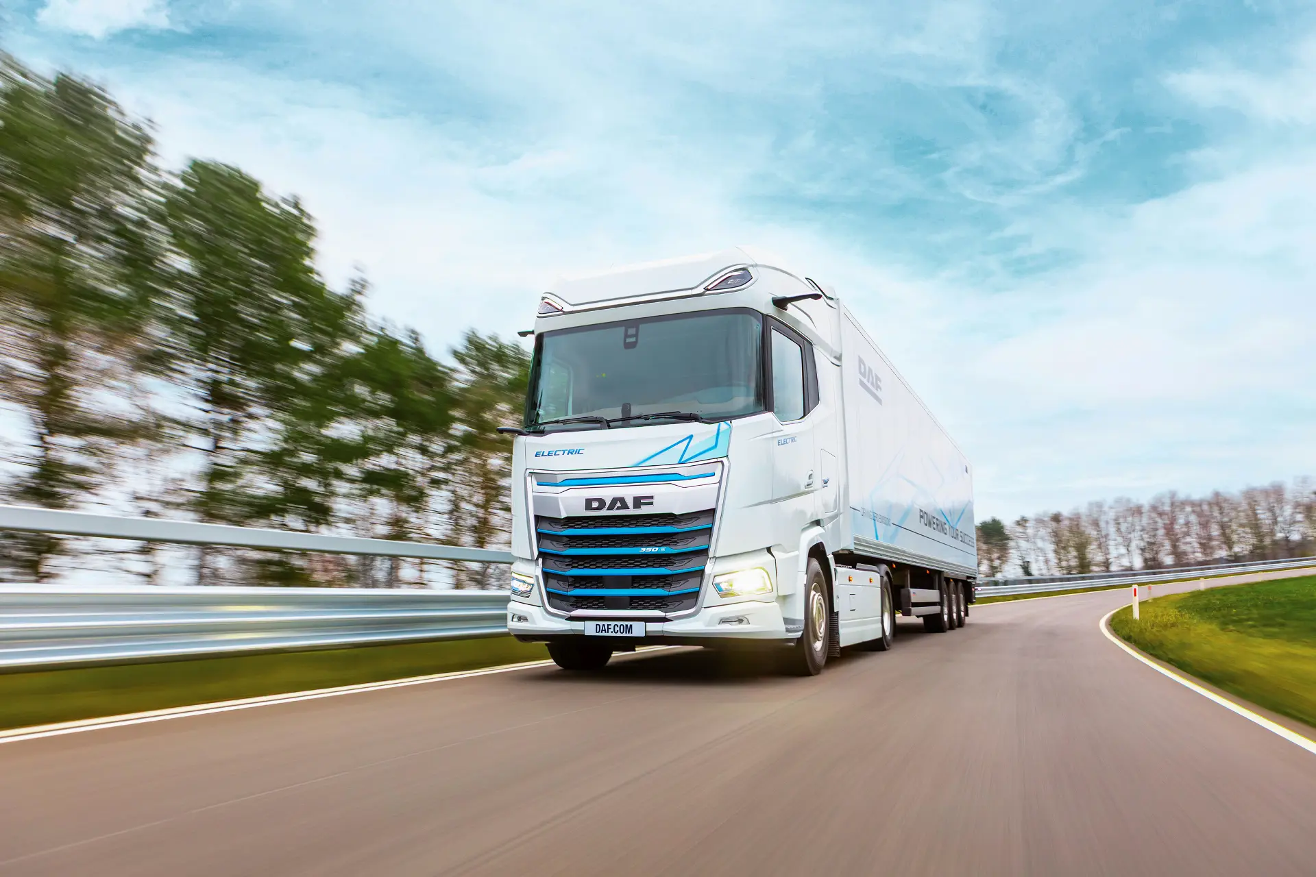Un camión eléctrico DAF blanco circula por una carretera curva con árboles y un cielo azul de fondo, mostrando el futuro de los camiones eléctricos en un entorno real digno de simulador de rutas.