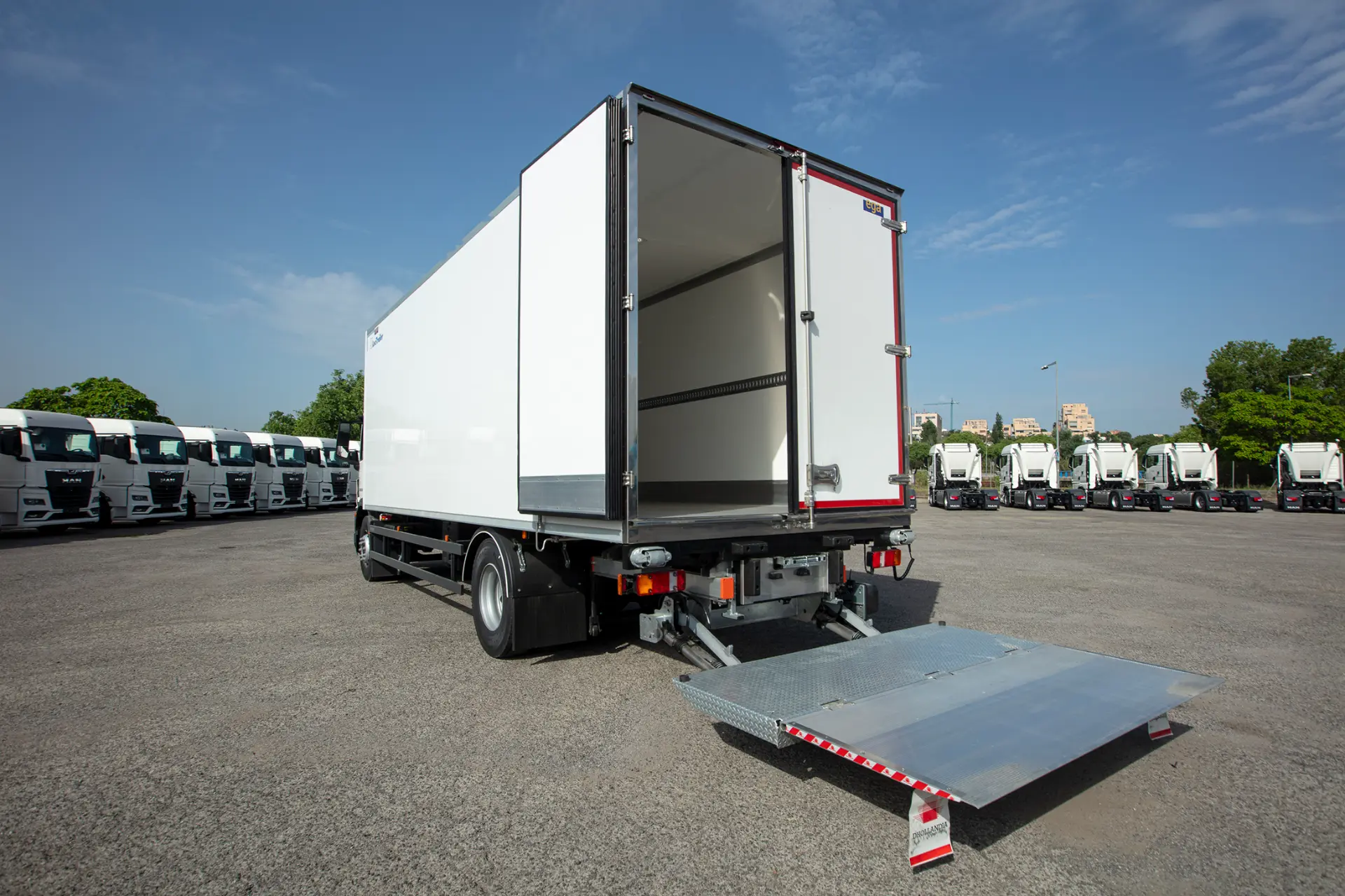 Un camión frigorífico MAN blanco con las puertas traseras abiertas y la compuerta metálica desplegada se encuentra en un aparcamiento, mostrando la calidad de los carroceros de MAN Truck & Bus Iberia.