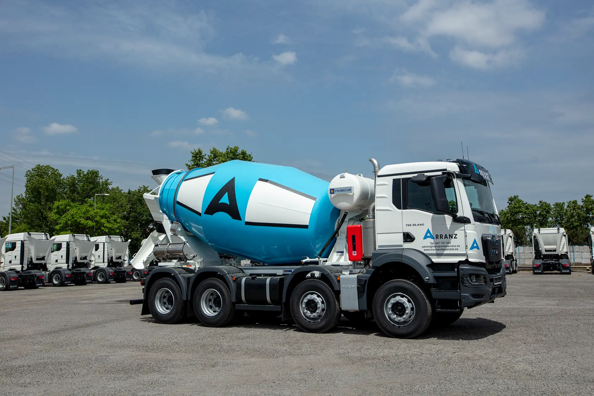 Una hormigonera MAN Truck & Bus Iberia azul y blanca, diseñada para carroceros y que ofrece una solución 360, está aparcada en un solar bajo un cielo parcialmente nublado.