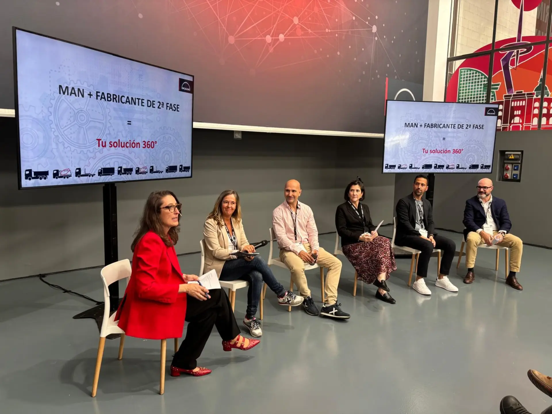 Seis personas se sientan en un escenario con dos grandes pantallas que muestran "MAN + FABRICANTE DE 2ª FASE", donde se habla de los vehículos rígidos MAN y de las innovaciones de MAN Truck & Bus Iberia.