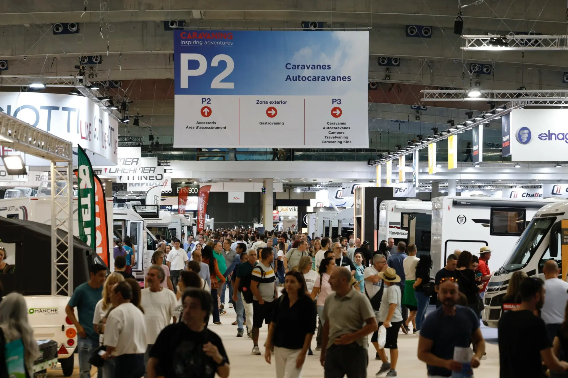 Una gran multitud recorre una sala de exposiciones cubierta, explorando vehículos recreativos bajo un gran cartel de caravanas, celebrando el espíritu del caravaning en España.