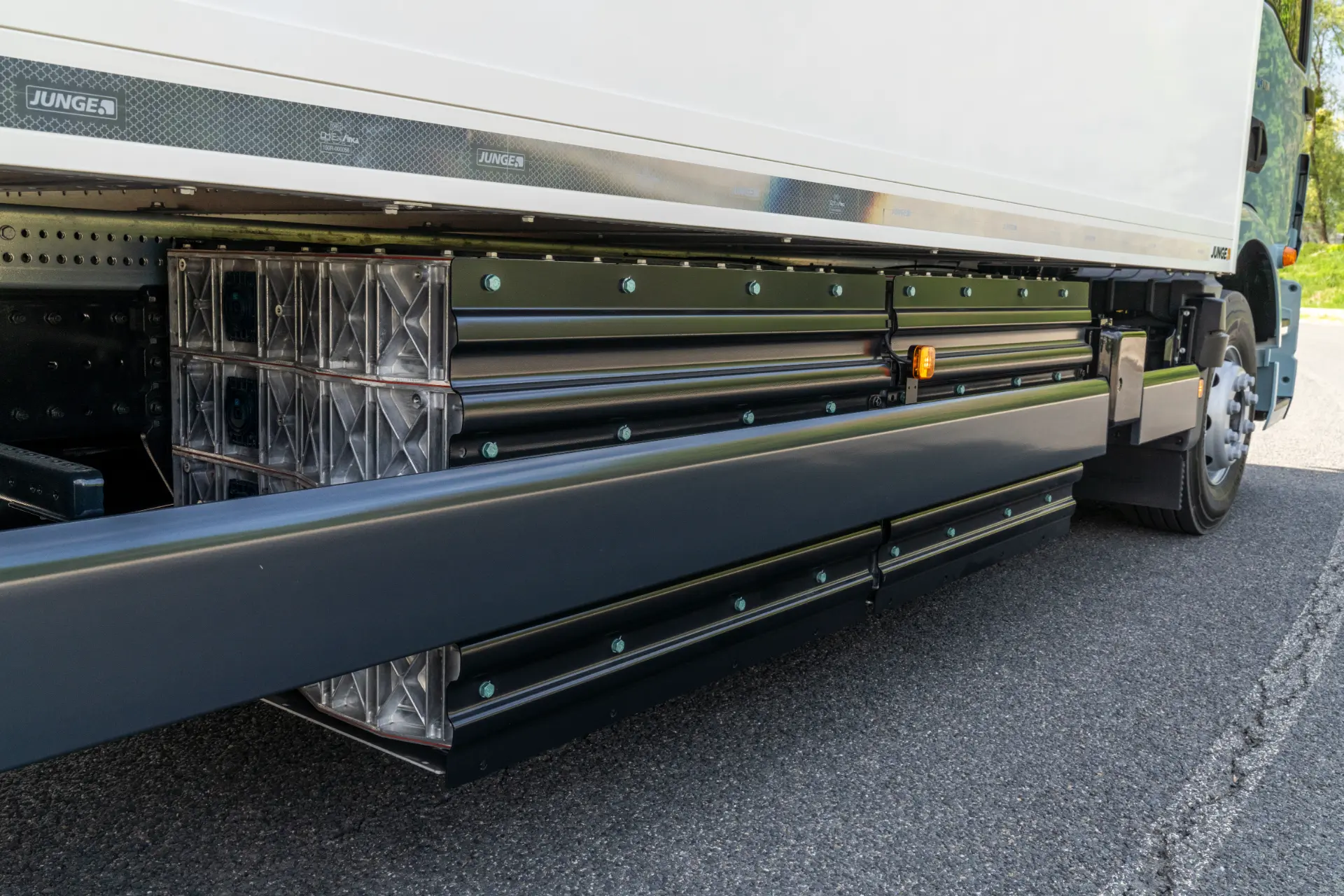 Primer plano de la protección lateral antiempotramiento de un camión con paneles reflectantes y elementos de seguridad, incluido un sistema Borrador automático, estacionado sobre asfalto.