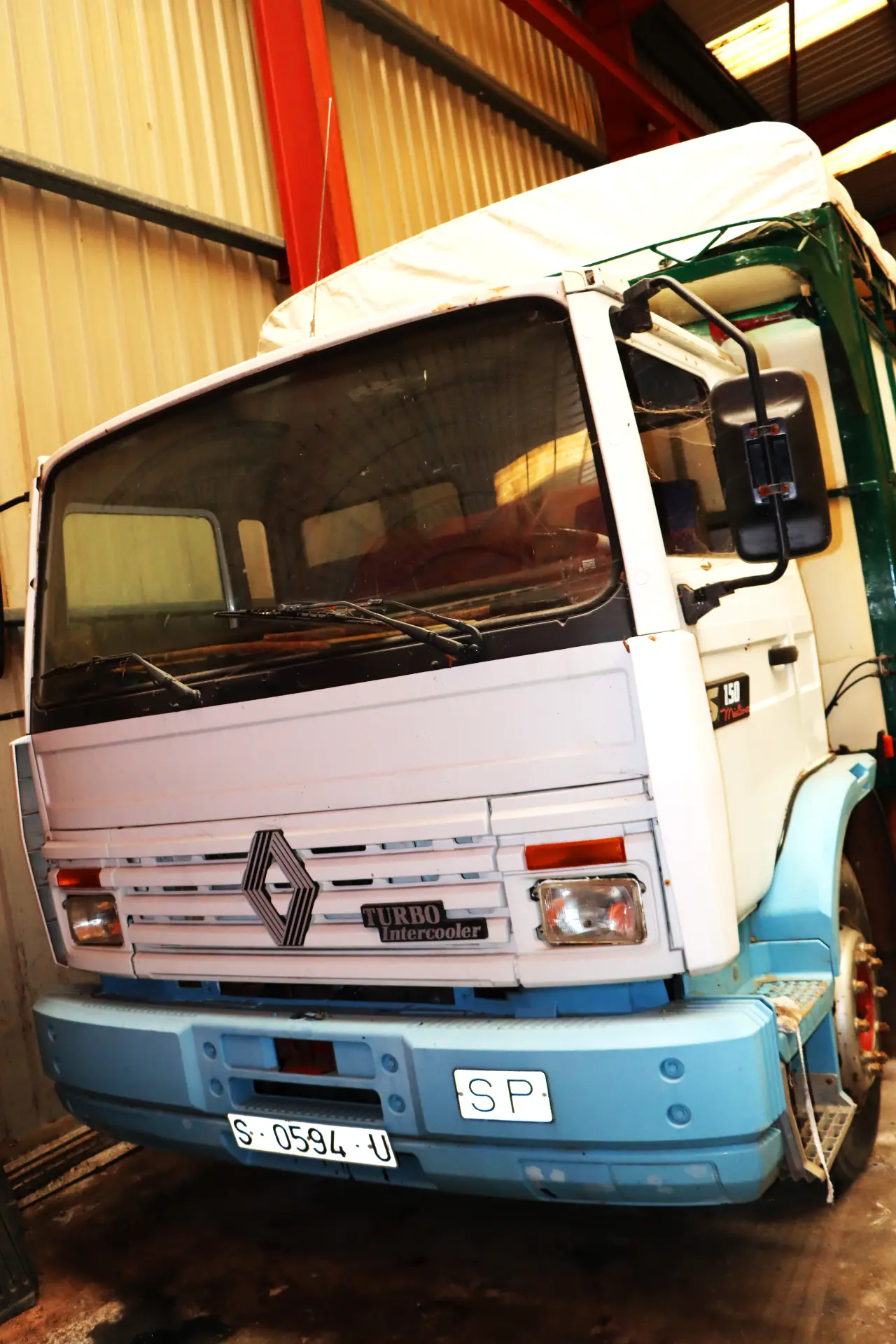 Un camión Renault blanco y azul, uno de los camiones clásicos, está aparcado en el interior de un garaje industrial.