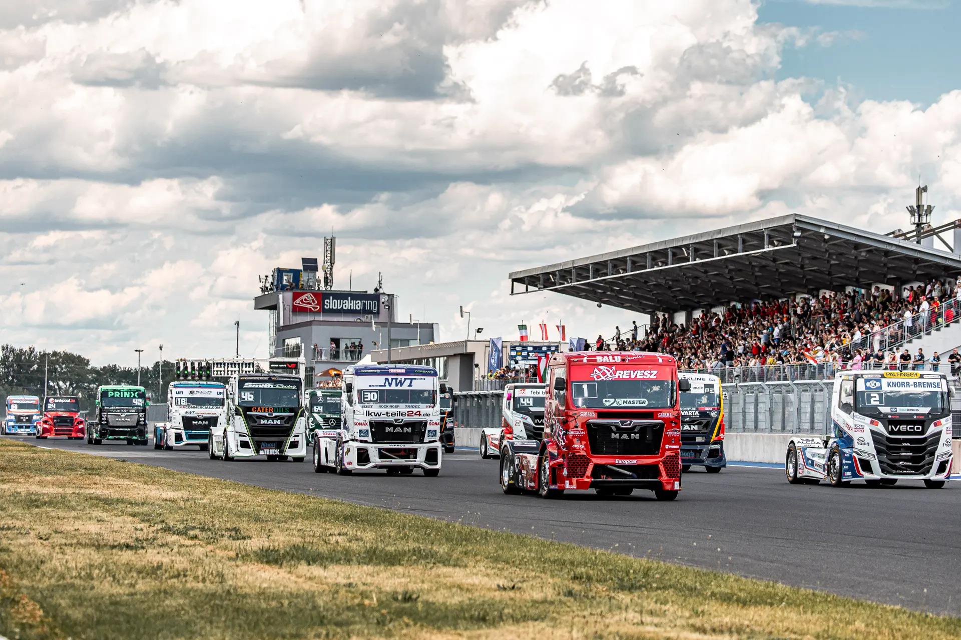 Carrera de camiones en marcha en el circuito de Eslovaquia, parte del Europeo de Camiones, con una grada llena de espectadores al fondo animando a Kiss.