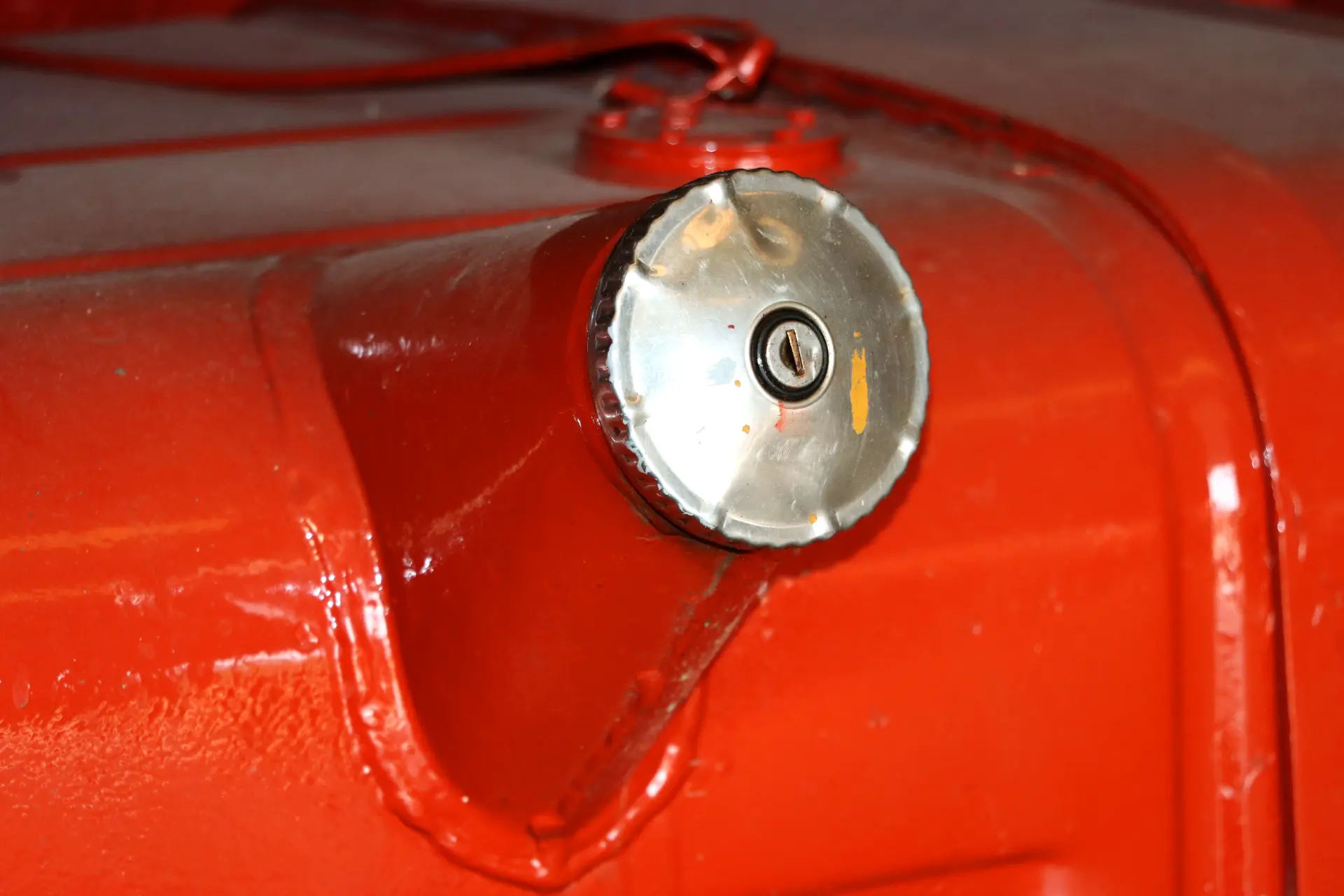 Primer plano de un tapón metálico del depósito de gasolina con el ojo de la cerradura visible en la superficie roja de un camión Barreiros, que destaca el diseño atemporal de los camiones clásicos.