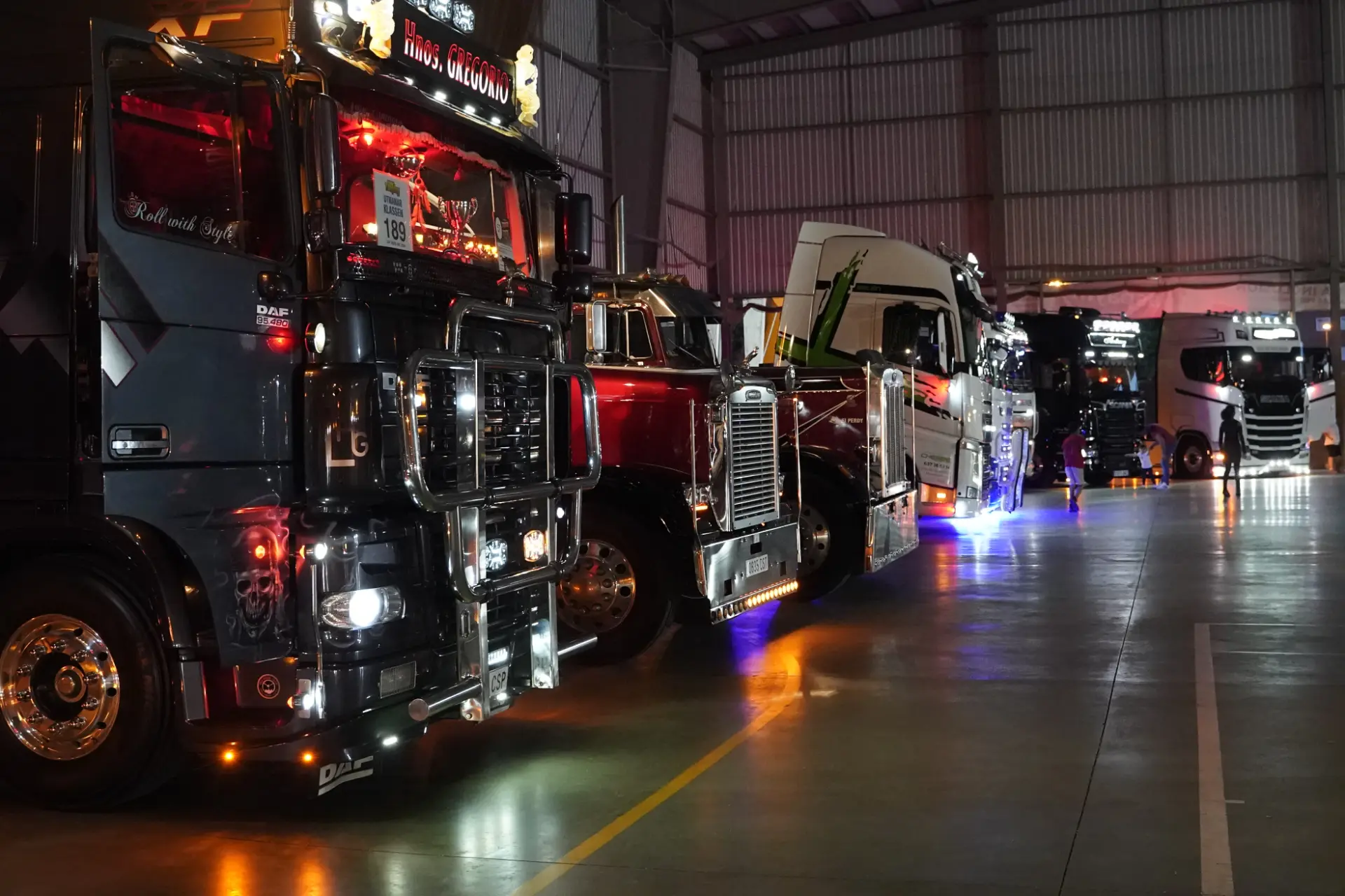 Fila de vehículos personalizados brillantemente iluminados aparcados en el interior con luces de colores debajo de cada camión en una concentración solidaria de camiones en Ávila.