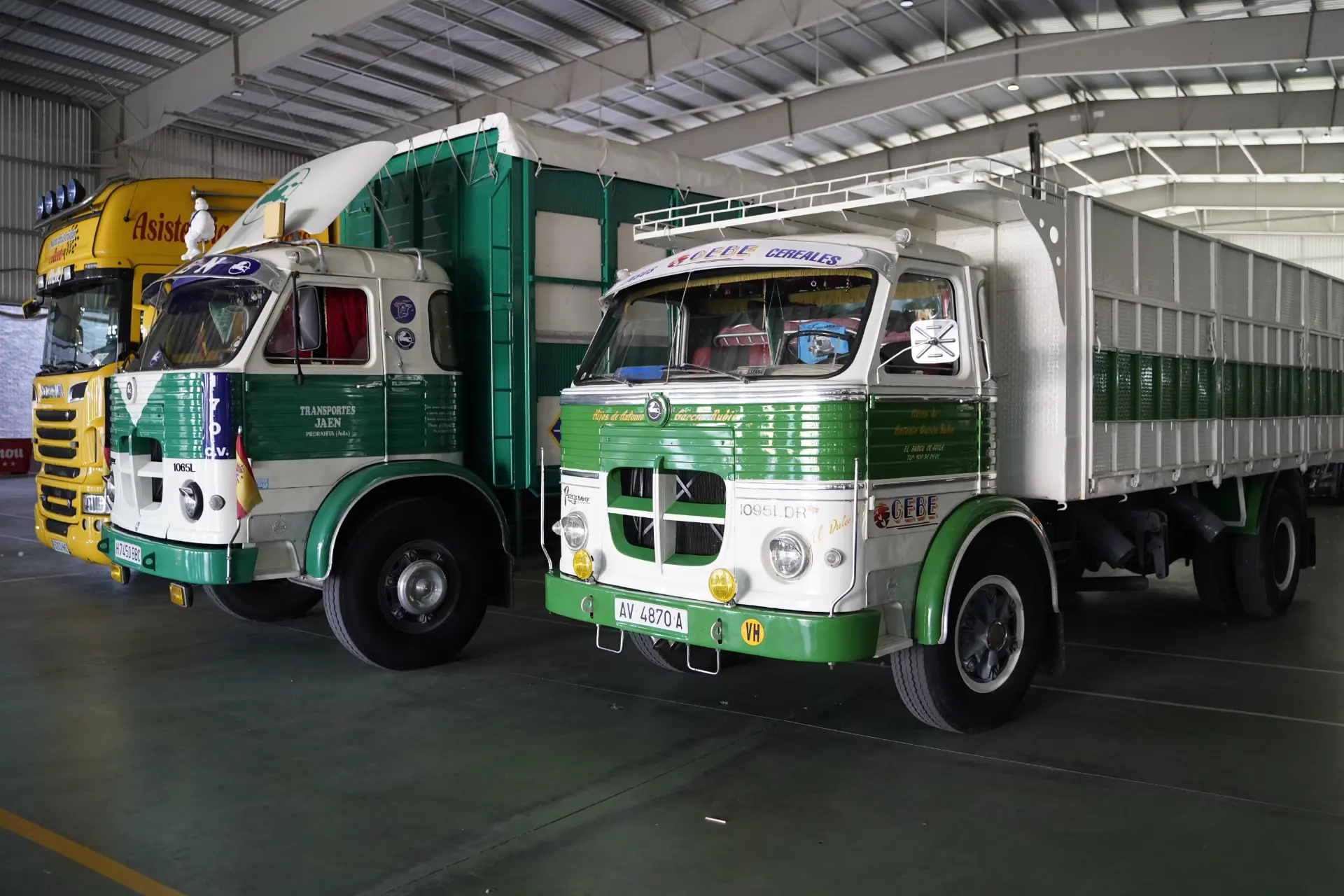 Dos camiones antiguos, verdes y blancos, aparcados en un garaje bien iluminado, listos para la concentración solidaria de Ávila.