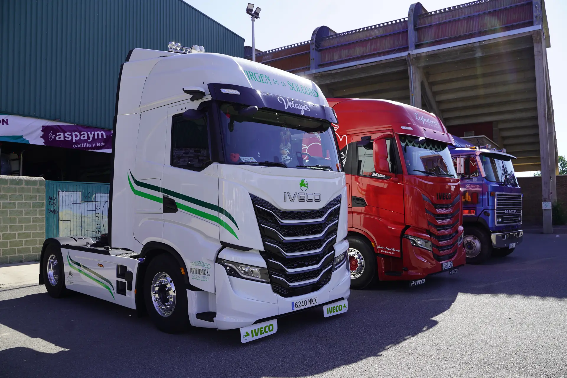 Tres coloridos semirremolques Iveco -blanco, rojo y azul- aparcados uno junto al otro en un soleado solar durante una concentración solidaria de camiones en Ávila.