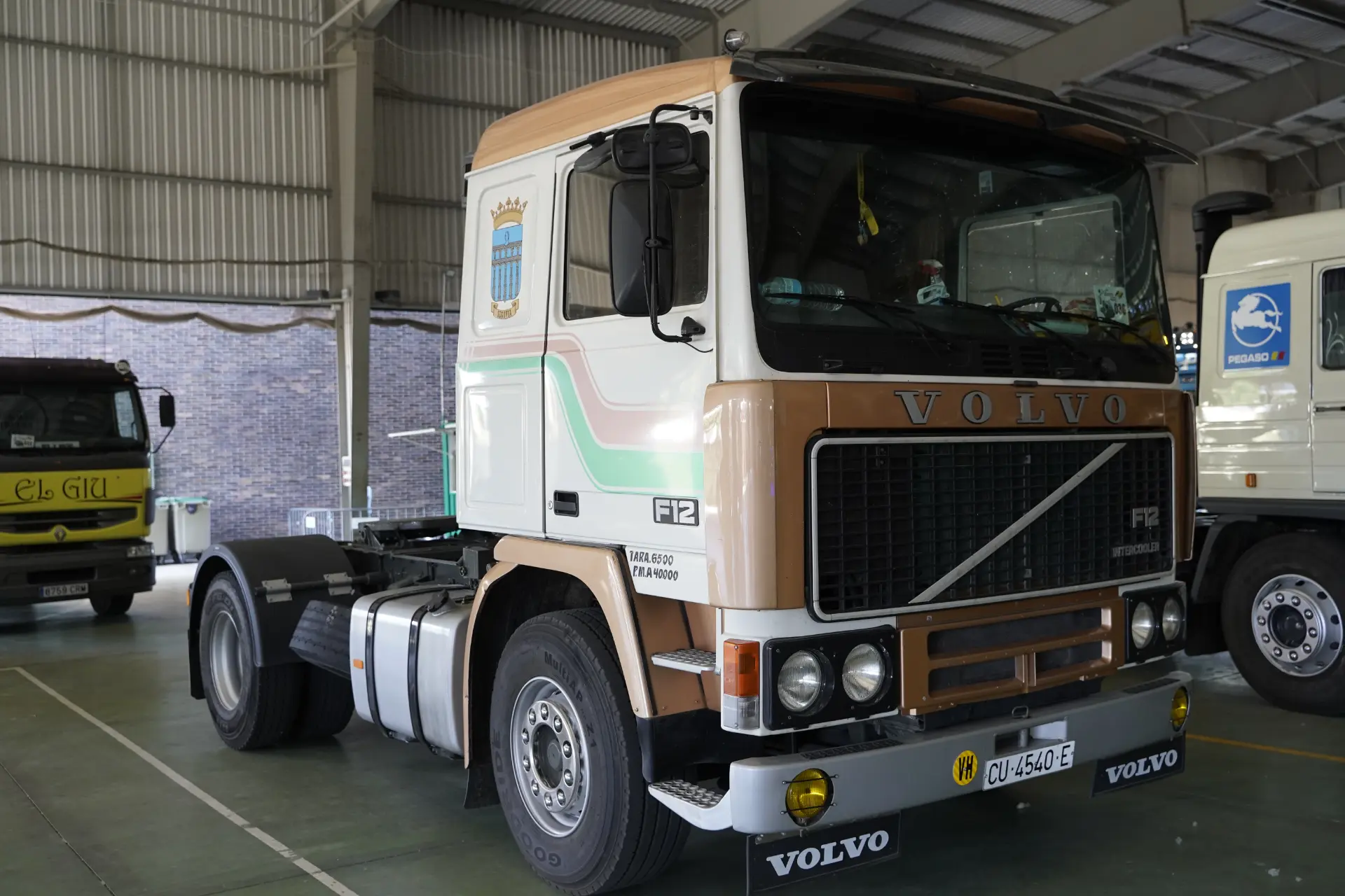 Un camión Volvo F12 de época con cabina marrón y blanca aparcado en el interior, junto a otro camión, en la concentración solidaria de camiones en Ávila, donde se reunieron 95 vehículos.
