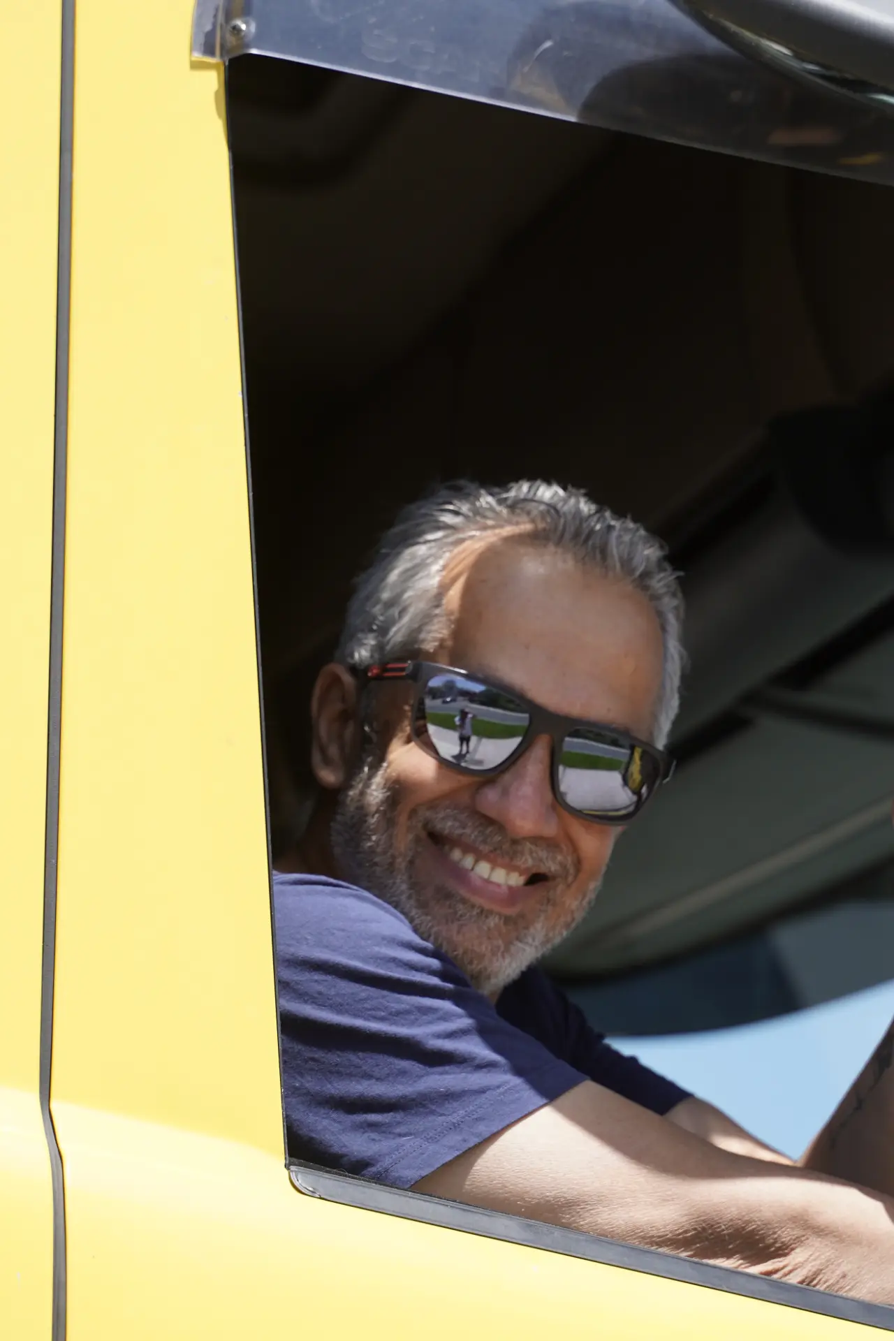 Un hombre sonriente con el pelo canoso y gafas de sol se asoma a la ventanilla de un vehículo amarillo durante la concentración solidaria de camiones en Ávila.