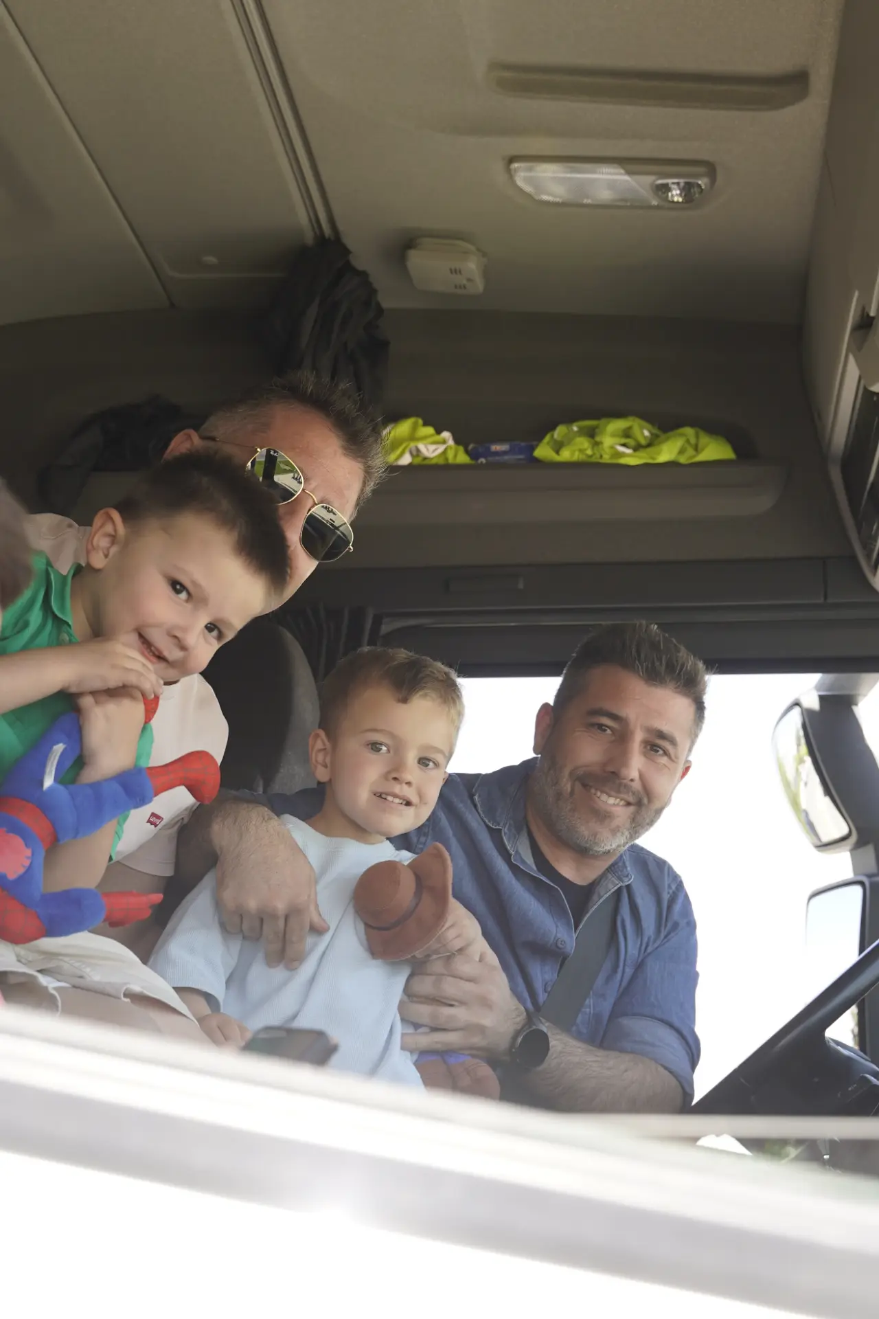 Dos hombres y dos niños sonríen juntos en el interior de un vehículo, posiblemente un camión, en una concentración solidaria de camiones en Ávila.