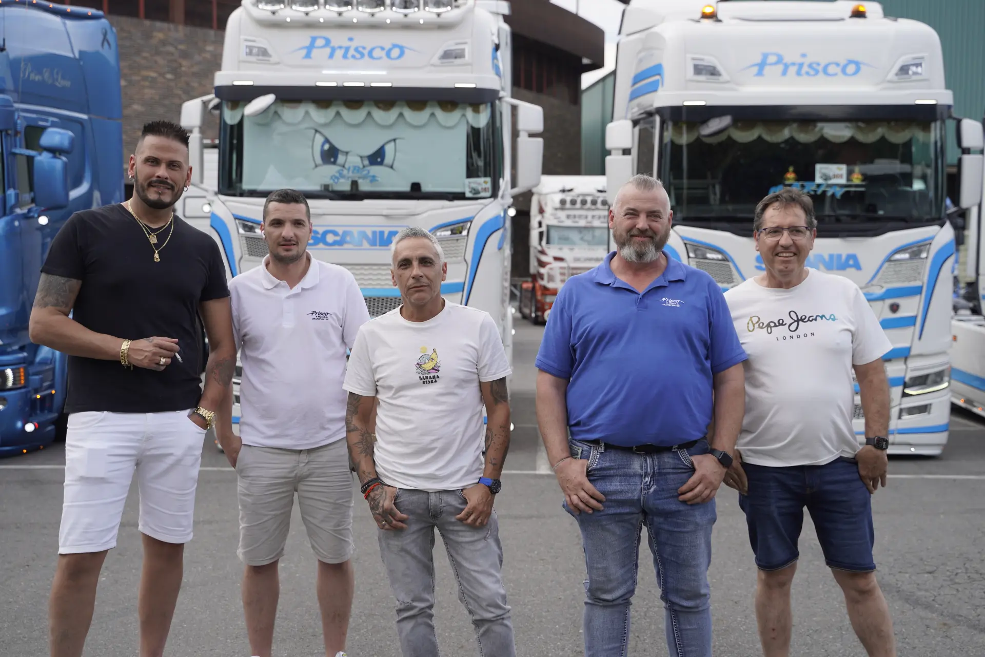 Cinco hombres posan delante de dos grandes camiones blancos con detalles azules, reunidos para la concentración solidaria de camiones en Ávila.