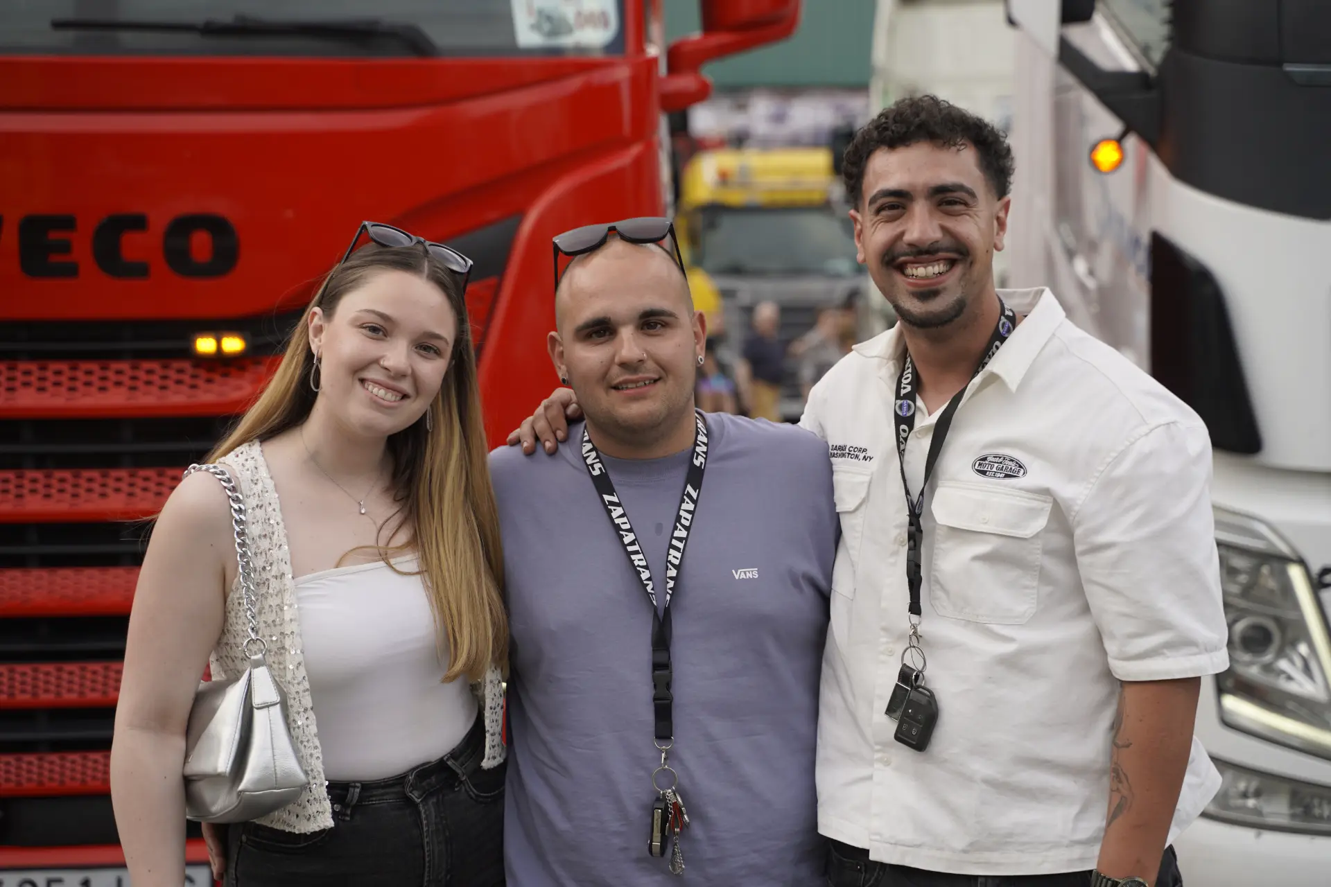 Tres personas sonríen y posan juntas frente a un camión rojo y otro blanco durante una concentración solidaria de camiones en Ávila.
