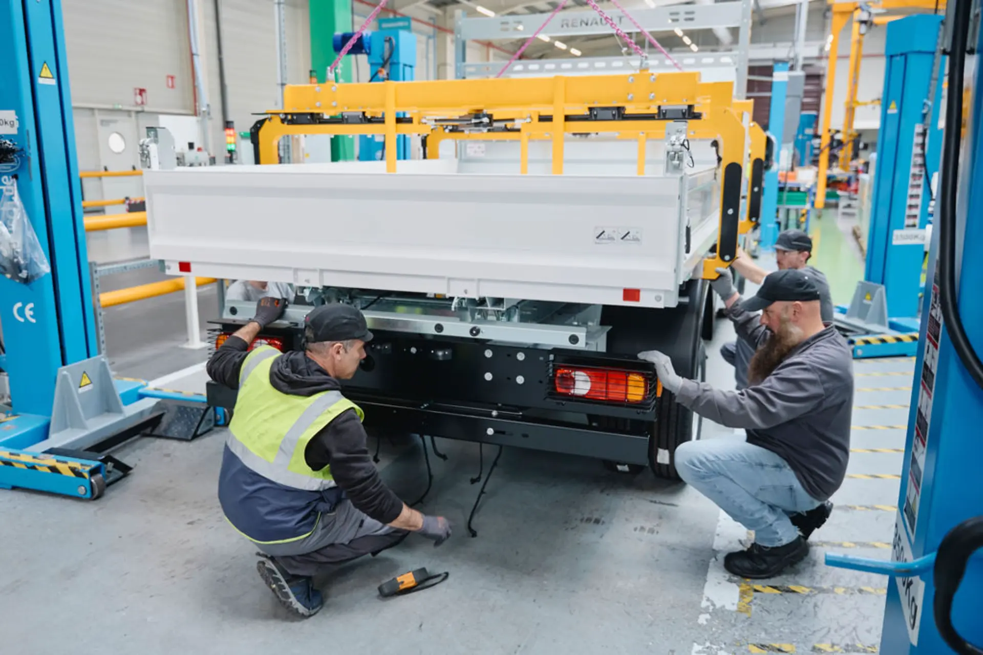 Tres trabajadores montan la parte trasera de un vehículo utilitario Renault, mostrando las transformaciones en la fábrica, en un luminoso entorno industrial.