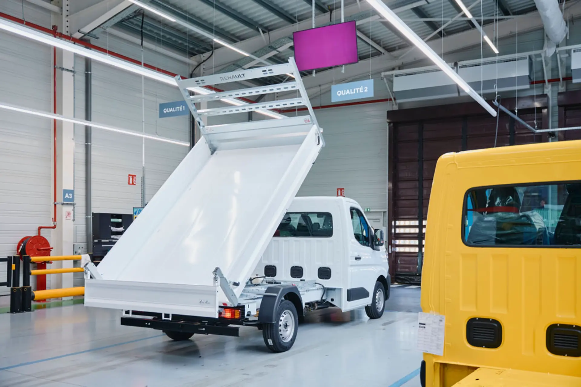 Una furgoneta comercial Renault blanca con la plataforma trasera elevada en una fábrica muy iluminada, en la que se muestran las transformaciones en fábrica de vehículos industriales.