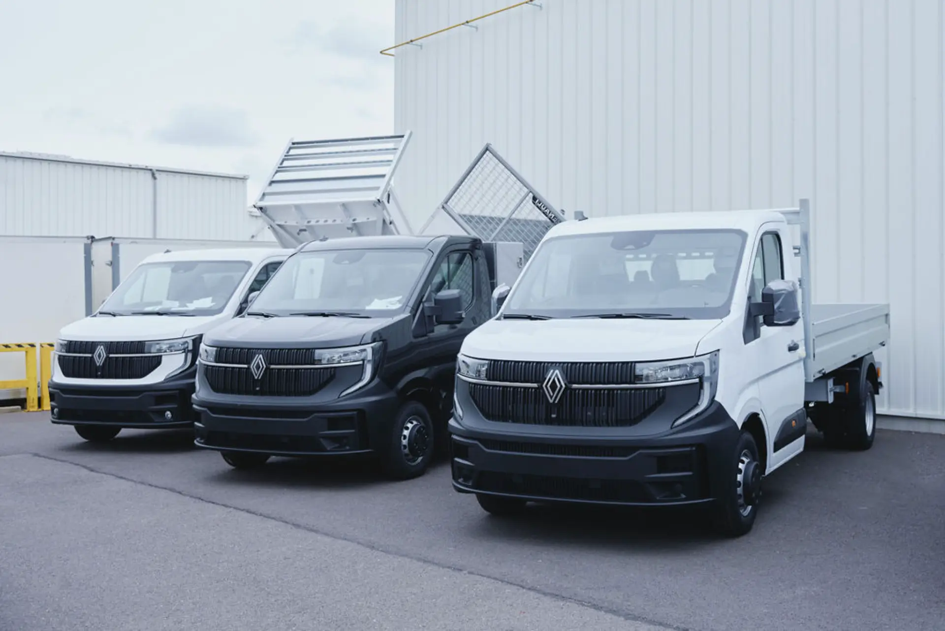 Tres modernas furgonetas Renault, vehículos industriales transformados por Renault, están aparcadas una al lado de otra en un terreno pavimentado junto a un edificio industrial blanco.
