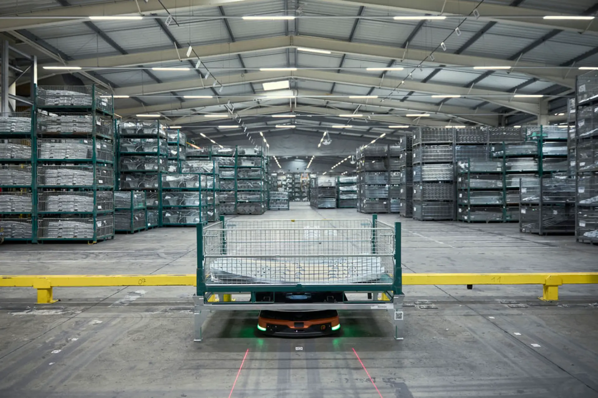Un almacén en Batilly con estanterías metálicas apiladas y un carro robotizado que transporta materiales por el suelo, dando apoyo a la producción del Renault Master.