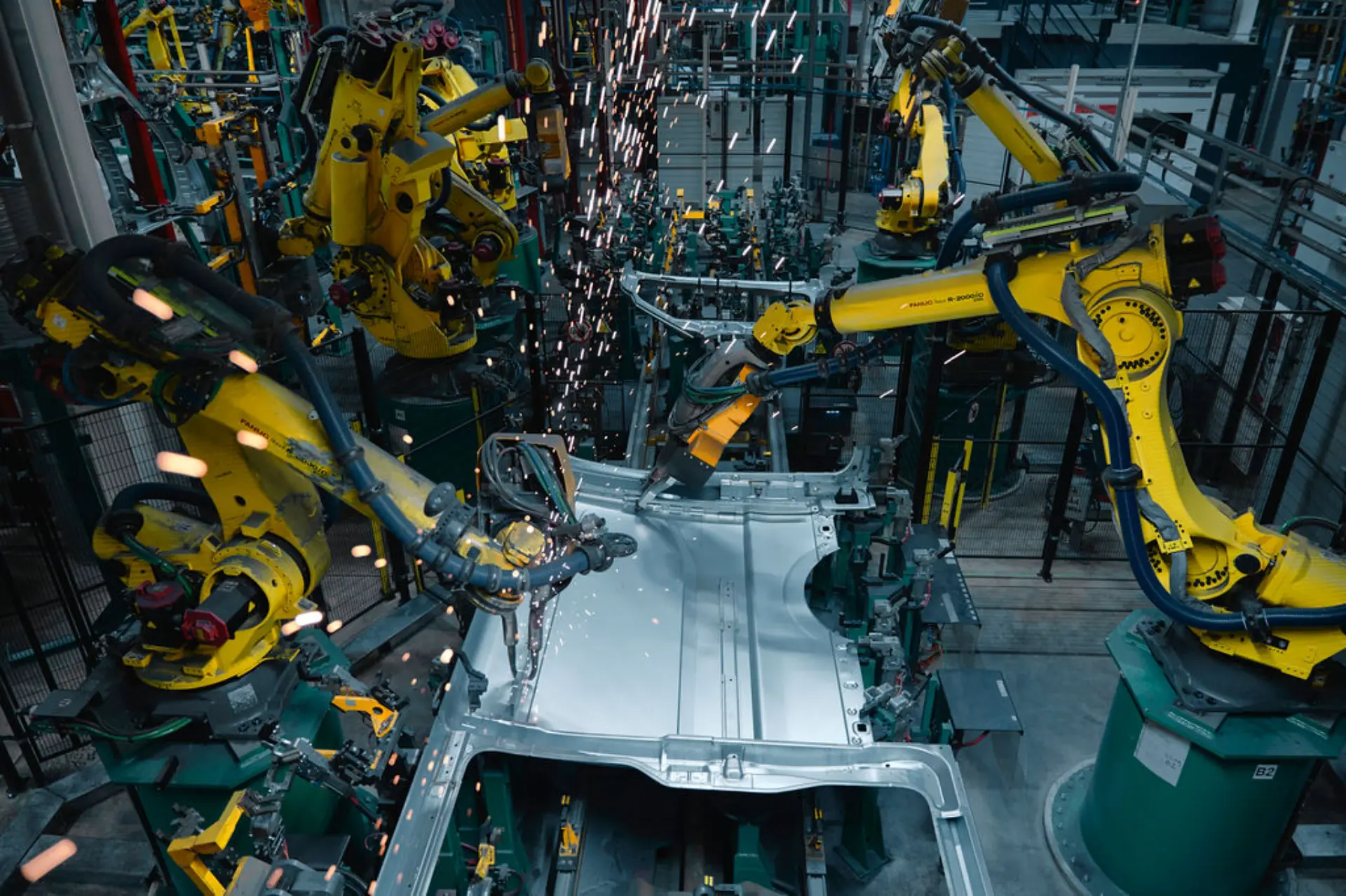 Robots industriales amarillos soldando y montando el chasis metálico de una Renault Master, con chispas volando en una fábrica de Batilly.