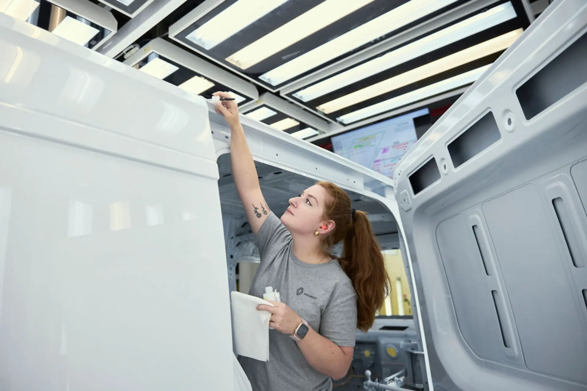 Una mujer revisa y retoca la pintura de una Renault Master blanca en un taller muy bien iluminado de Batilly.