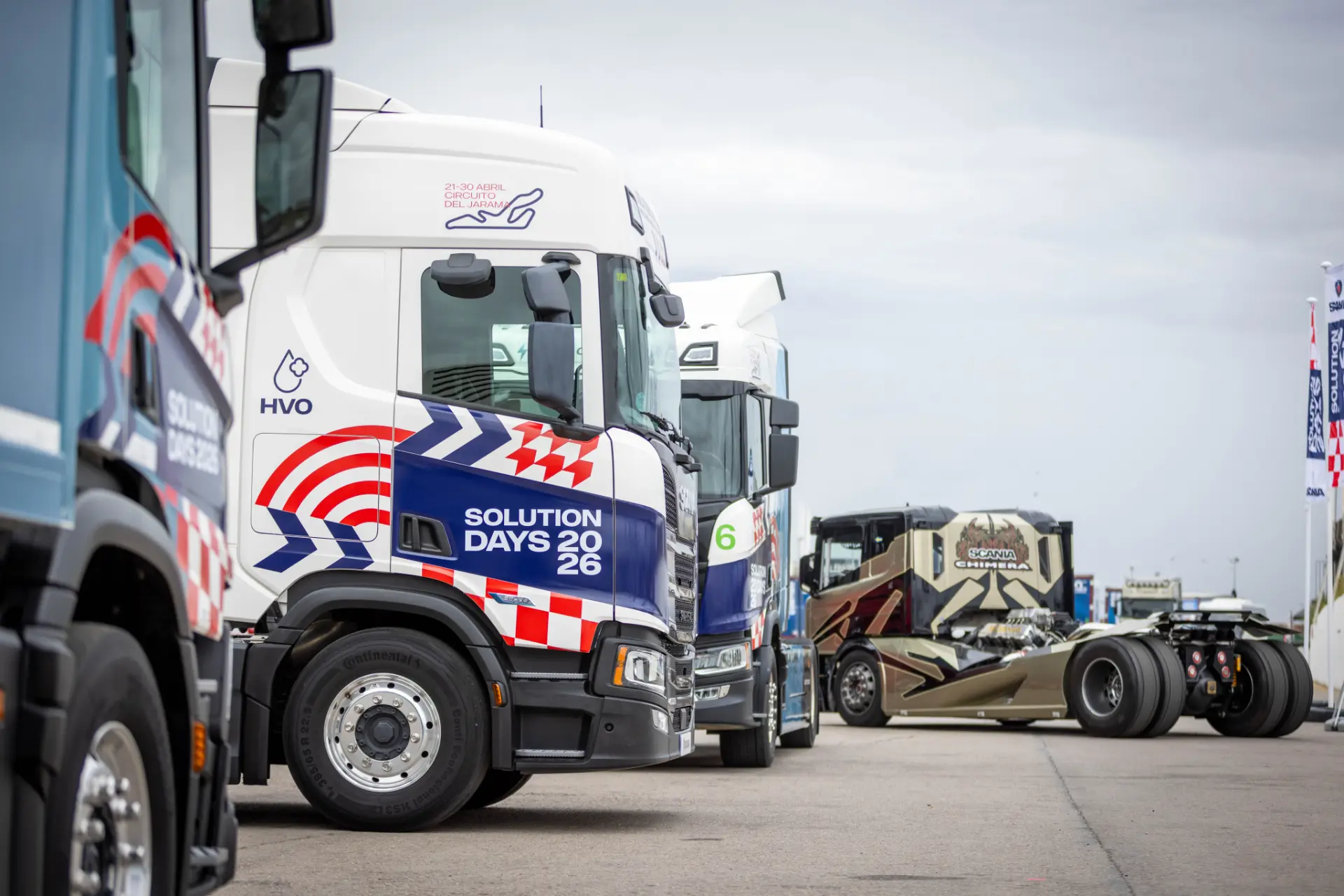 Una fila de camiones Scania aparcados en un terreno pavimentado durante los «Scania Solution Days», bajo un cielo nublado.
