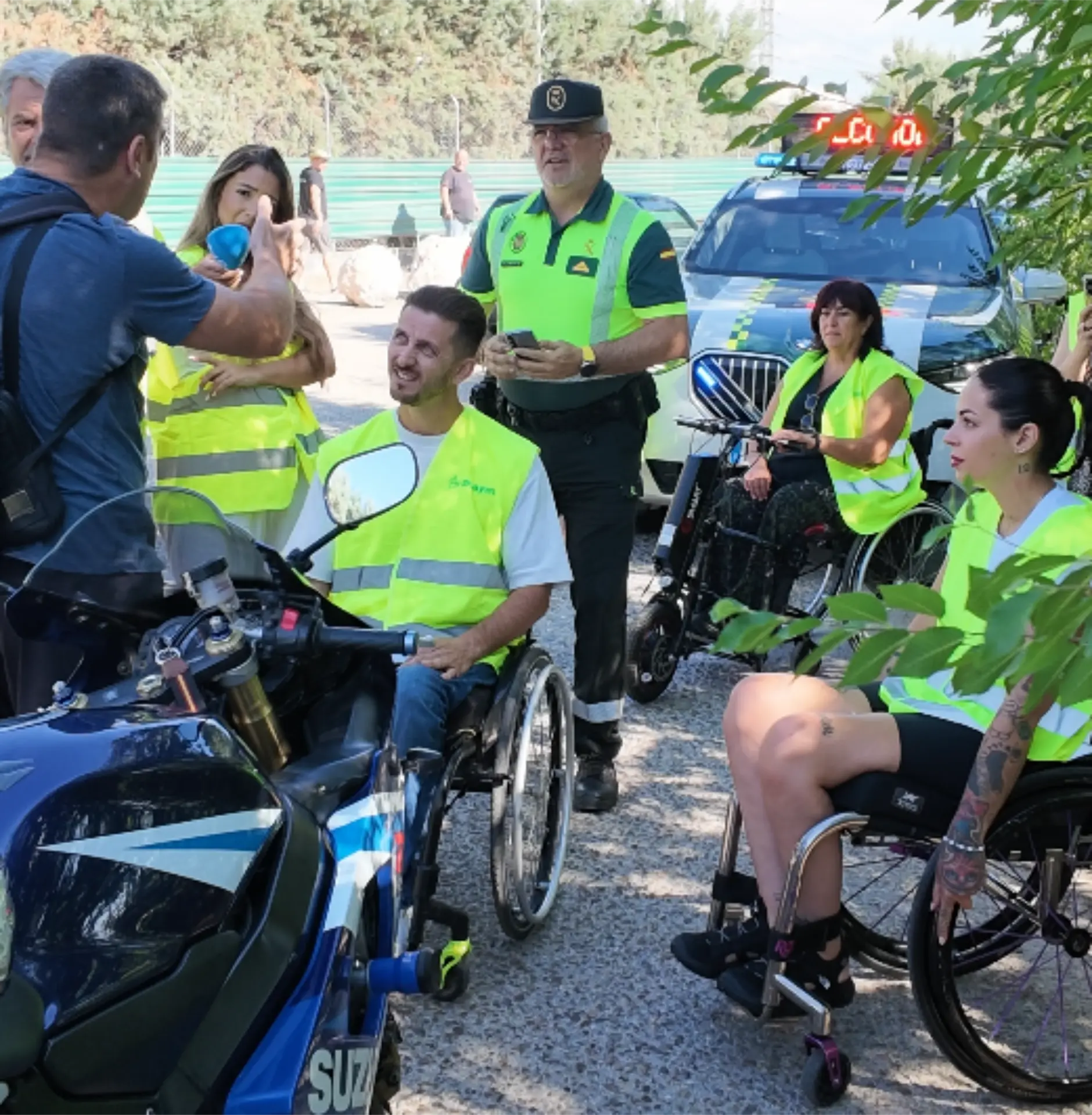 Unas personas en silla de ruedas y unos agentes de policía charlan junto a un coche patrulla y una moto en un día soleado, hablando sobre temas de seguridad vial y los peligros del alcohol al volante.
