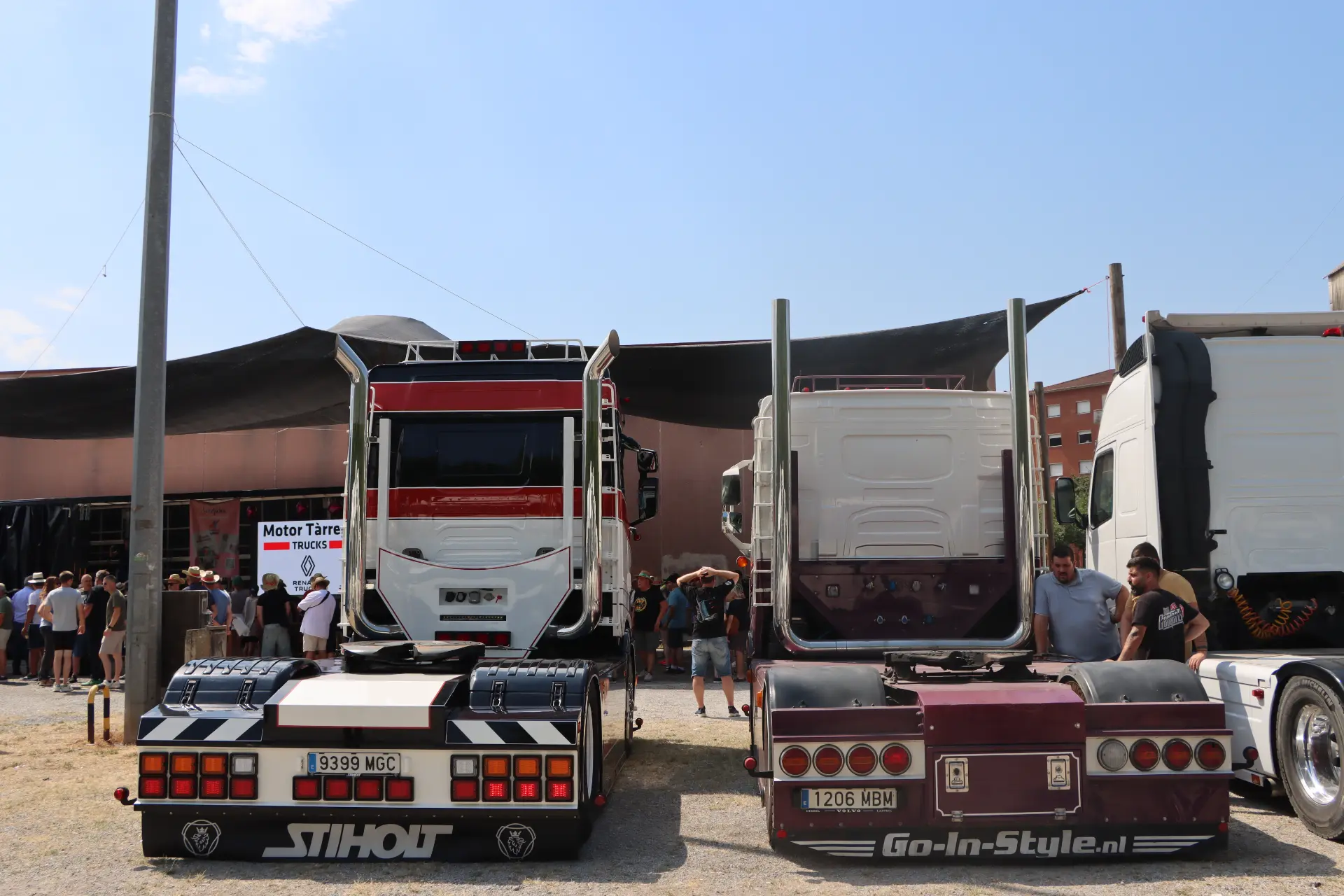 Dos camiones aparcados uno al lado del otro en un evento al aire libre, con gente reunida y un cartel al fondo; uno de ellos lucía con orgullo el logotipo del equipo «Truck Olot», lo que llamó la atención de los aficionados a los camiones y de los miembros de la comunidad de «Camiones de San Cristóbal».