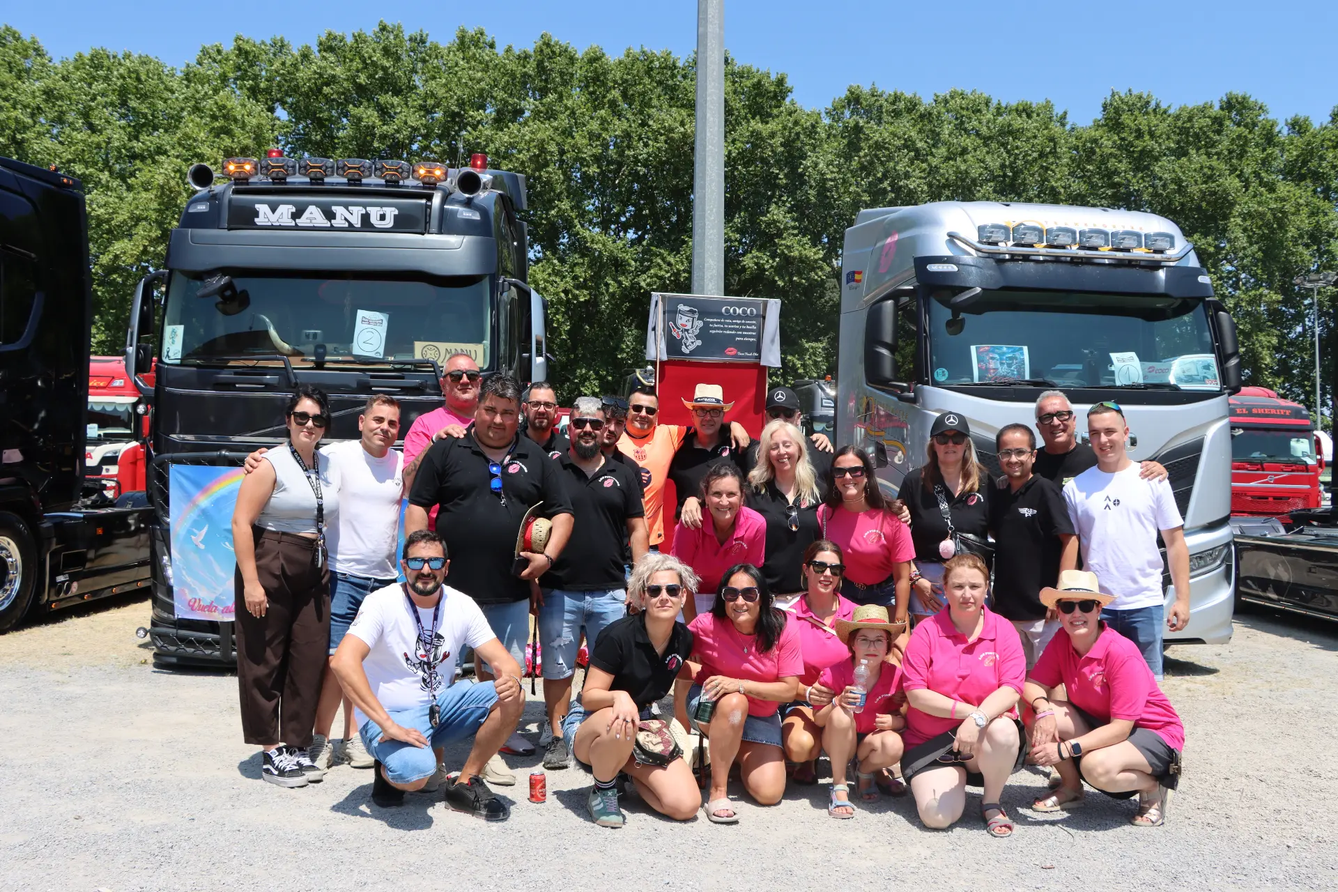 Un grupo de personas posa junto a dos grandes camiones en un día soleado, reunidas para rendir homenaje a Oti Cabadas con el espíritu vibrante de San Cristóbal Camiones.