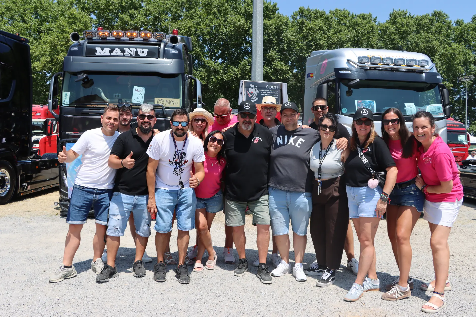 Un grupo de personas sonríe y posa junto a dos grandes camiones en un día soleado durante la concentración de camiones de Olot, reunidas como parte de un homenaje a Oti Cabadas.