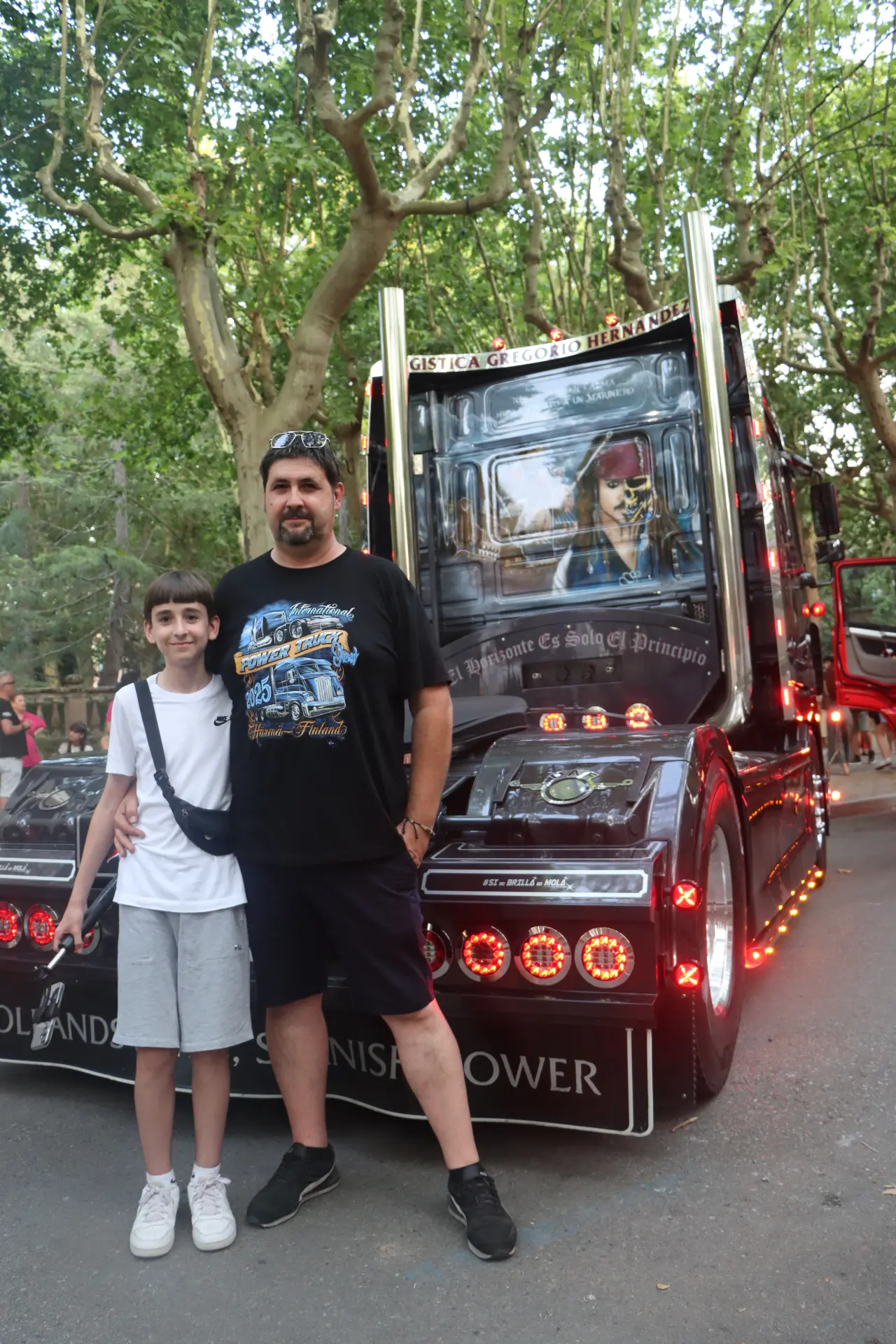 Un hombre y un niño posan delante de un camión decorado con motivos piratas y luces de colores, que forma parte de la impresionante concentración de camiones de equipo en Olot: un auténtico homenaje a Oti Cabadas.