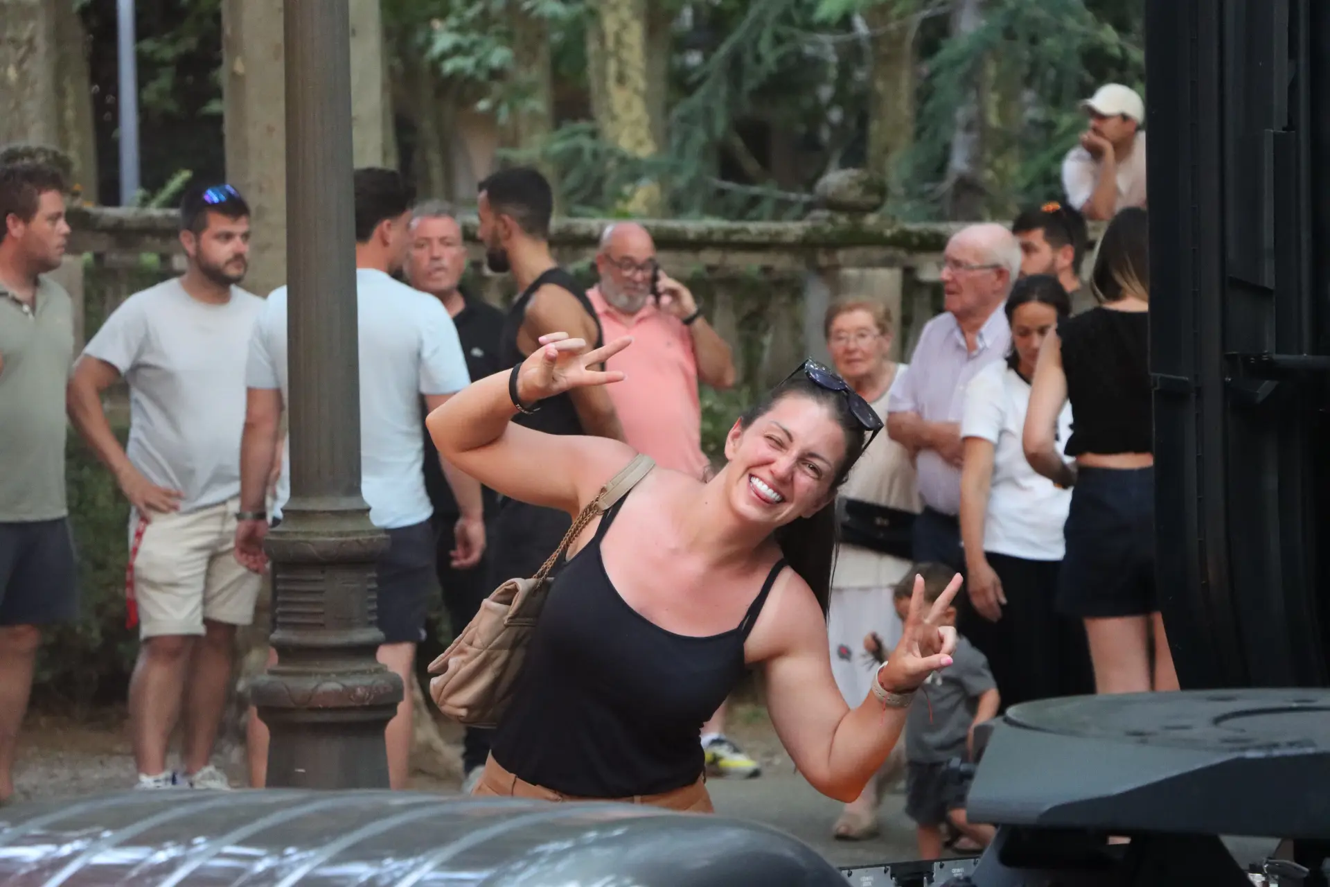 Una mujer sonriente, con un top negro, posa haciendo el signo de la paz en la concentración de camiones de Olot, rodeada de una animada multitud y, al fondo, de otros aficionados del Team Truck Olot.