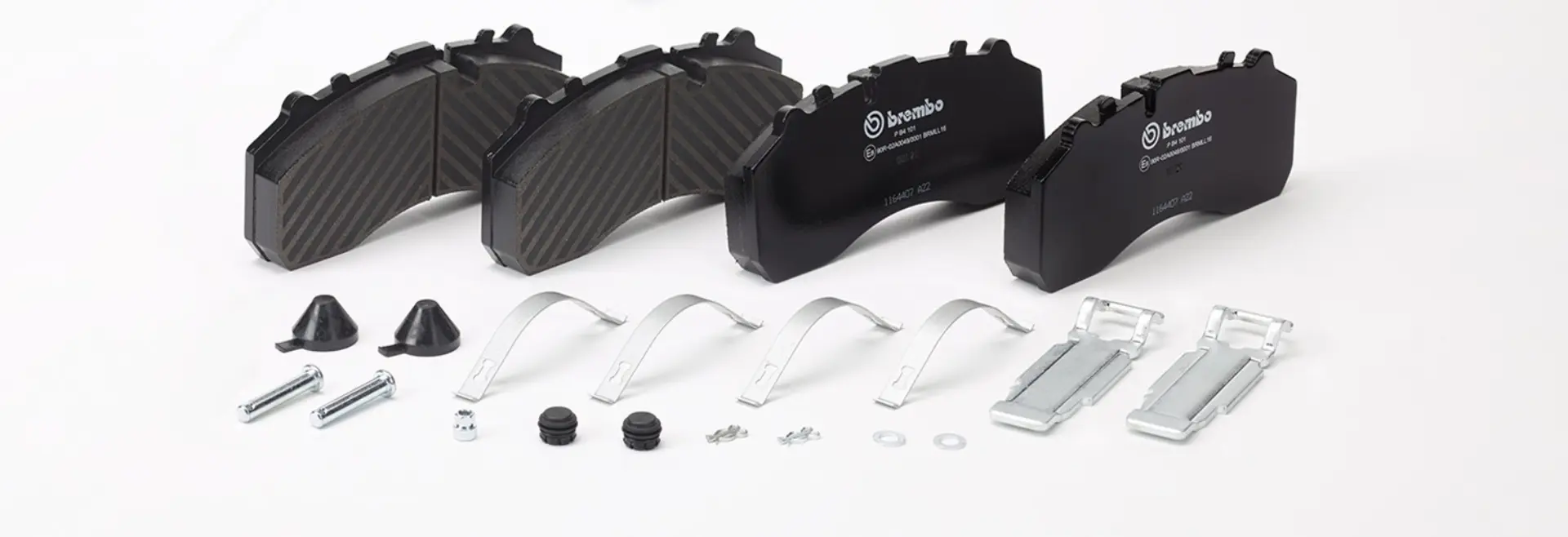 Cuatro pastillas de freno negras con los accesorios necesarios —incluidos clips, tornillos y tapones de goma—, dispuestas sobre una superficie blanca: ideales para los profesionales de la ingeniería de flotas que buscan optimizar la rentabilidad de las flotas y garantizar un mantenimiento eficiente.