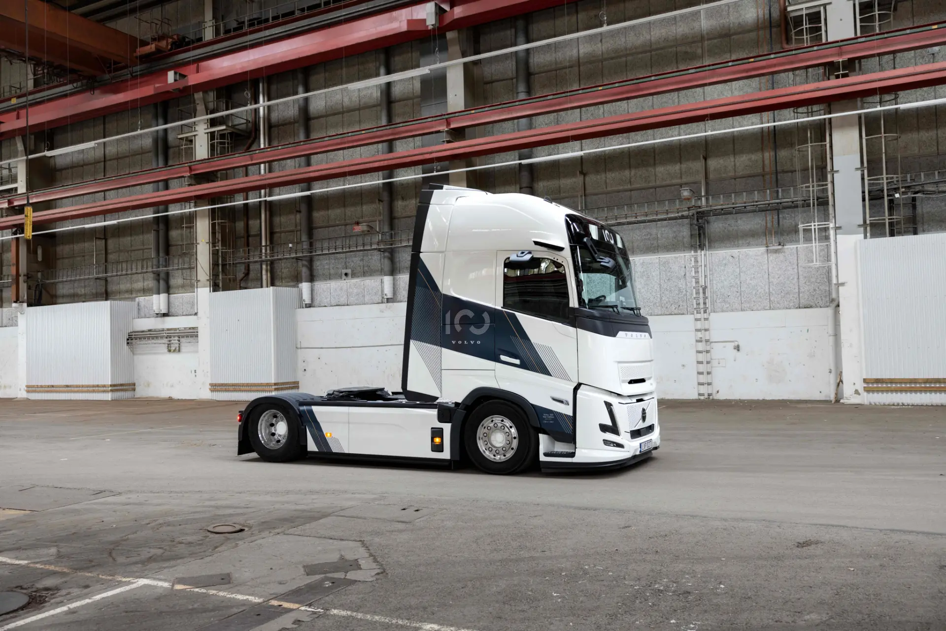 Cabina de un semirremolque Volvo FH16 Aero, de color blanco y azul, aparcada en el interior de una gran nave industrial vacía.