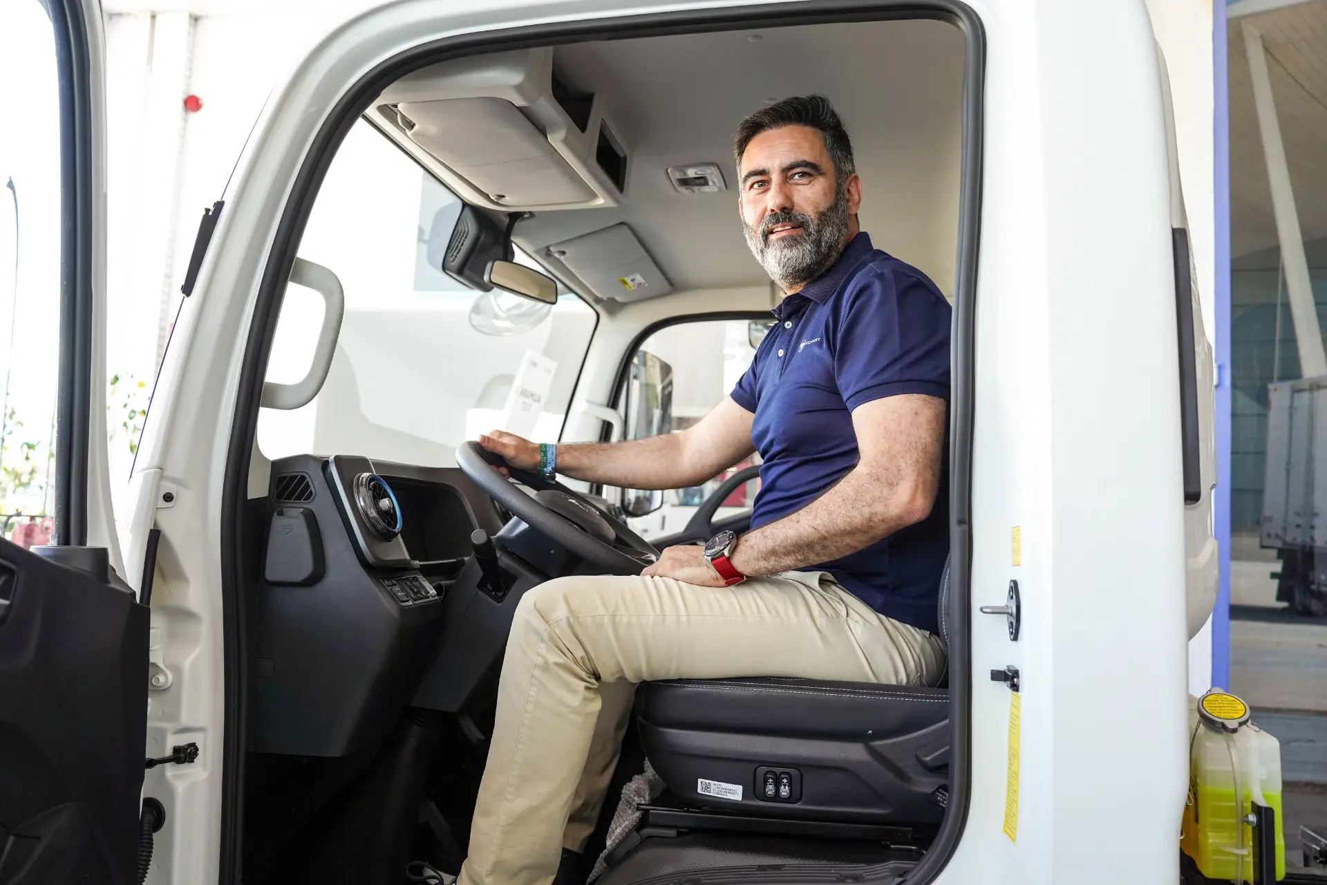 Un hombre con barba está sentado en el asiento del conductor de un camión Foton, mirando a la cámara y sonriendo.