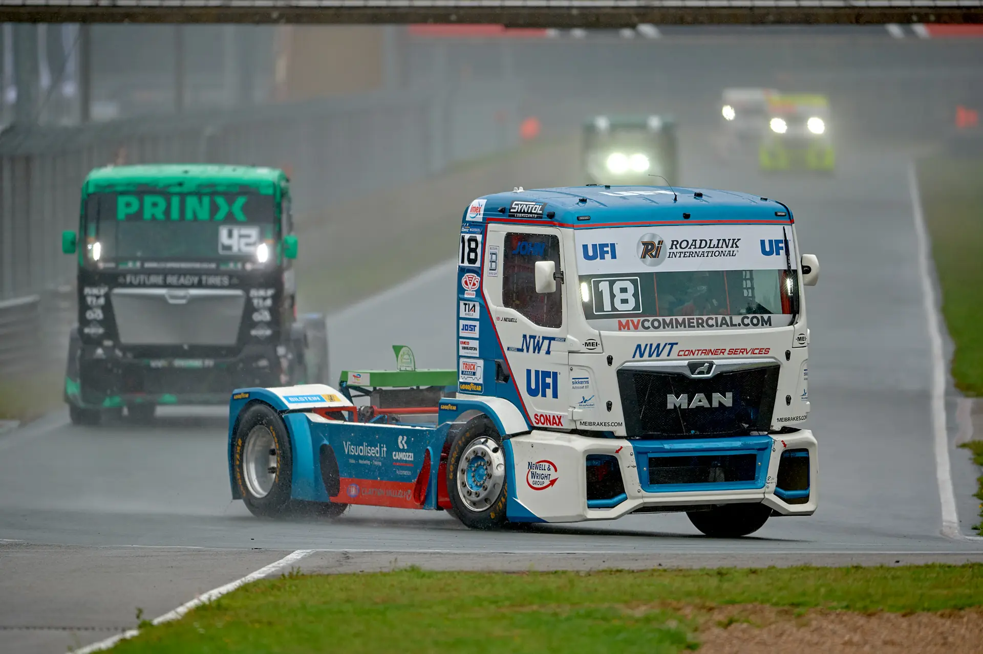 El camión de carreras azul y blanco n.º 18 lidera la carrera del Europeo de Camiones, disputada bajo la lluvia en Zolder, con Norbert Kiss dominando con destreza la pista mojada.