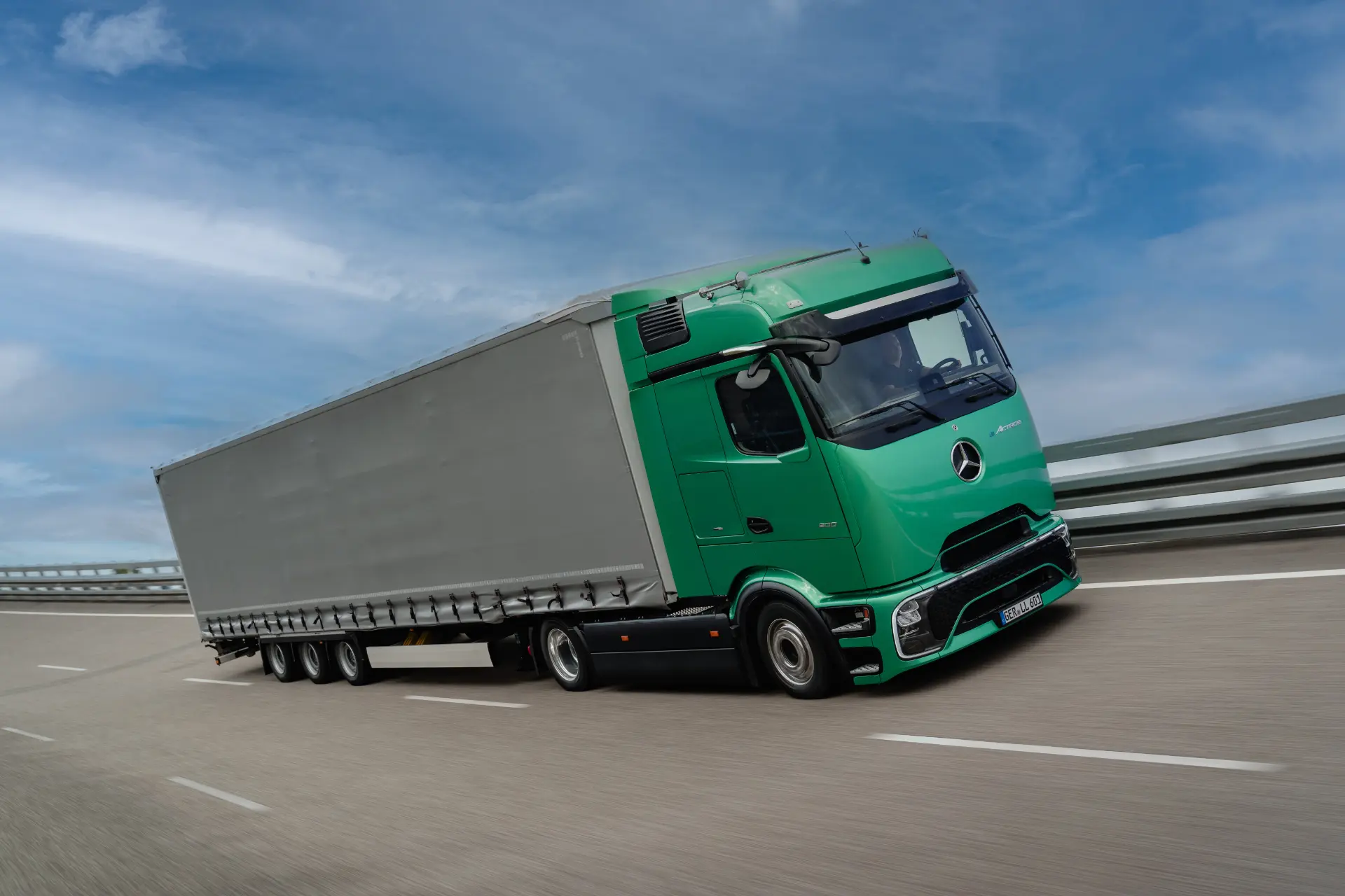 Un camión eléctrico Mercedes-Benz eActros 600 de color verde circula por una autopista bajo un cielo azul con ligeras nubes, demostrando sus prestaciones en el transporte de gran volumen.