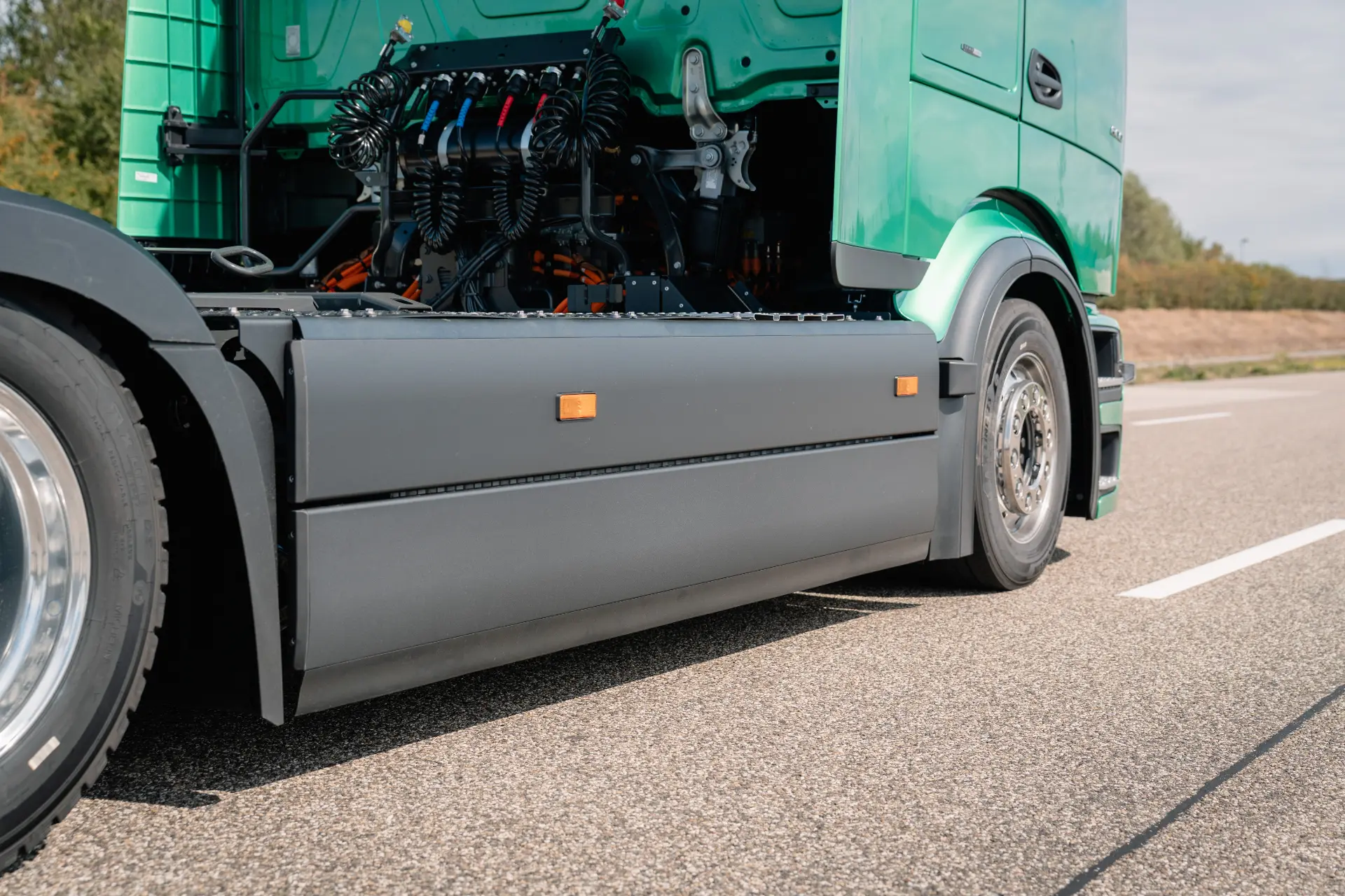 Primer plano de un Mercedes-Benz Trucks eActros 600 verde con la cabina levantada, dejando al descubierto el motor y los componentes, aparcado en una carretera.