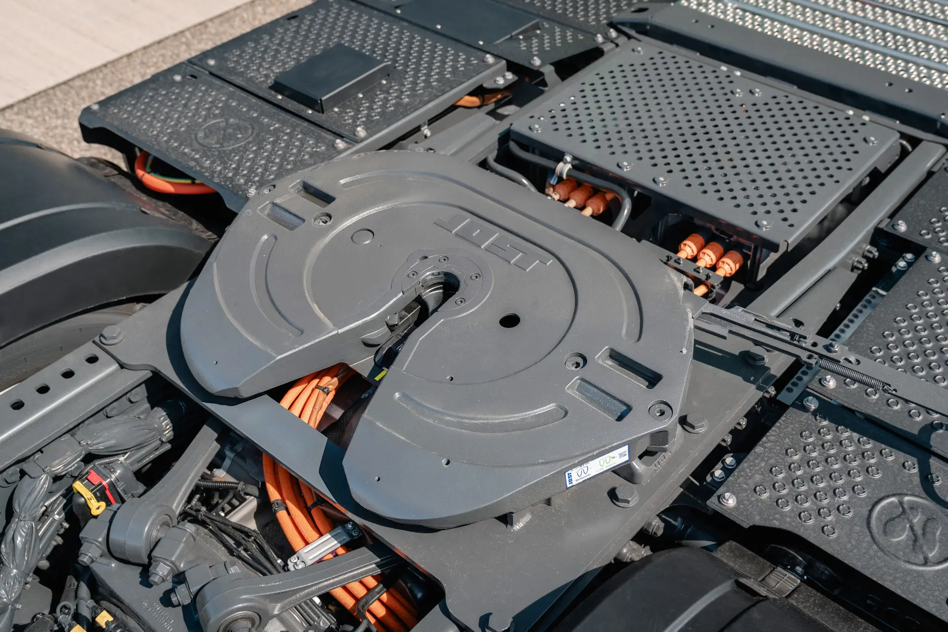 Primer plano de un acoplamiento de quinta rueda de Mercedes-Benz Trucks en un camión eléctrico, en el que se aprecian cables naranjas y paneles metálicos texturizados, característicos de los megatráileres modernos.