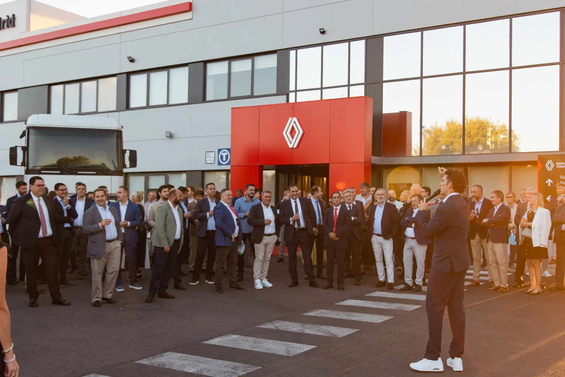 Un numeroso grupo de personas vestidas con traje de negocios se reúne frente a un edificio moderno con un letrero rojo de Renault, lo que pone de relieve la importancia de los servicios posventa para el transporte profesional en Getafe.