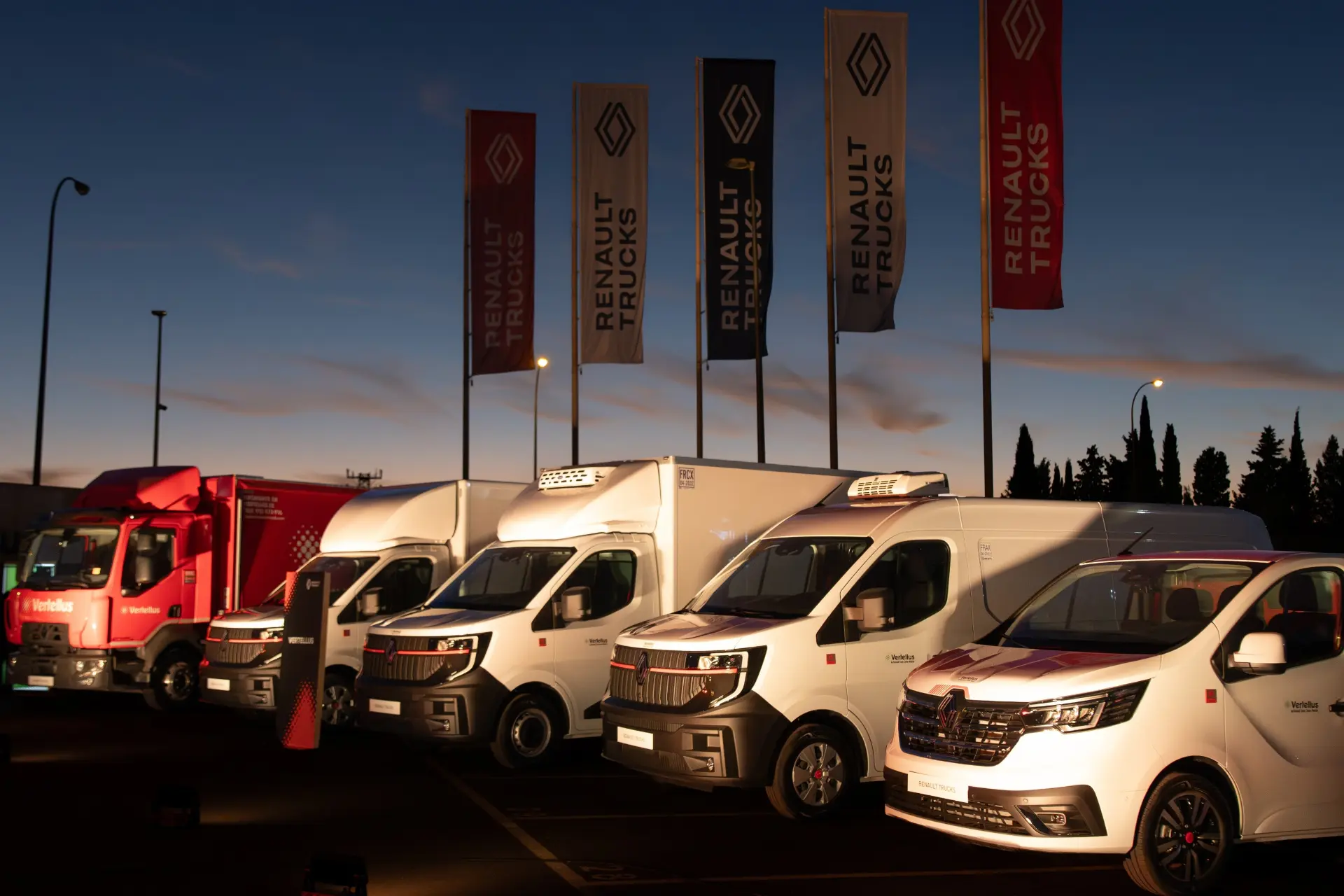 Al atardecer, una fila de furgonetas y camiones Renault está aparcada frente a las pancartas de Renault, lo que pone de relieve los fiables servicios posventa que ofrece Renault Trucks en el Truck Center Madrid.